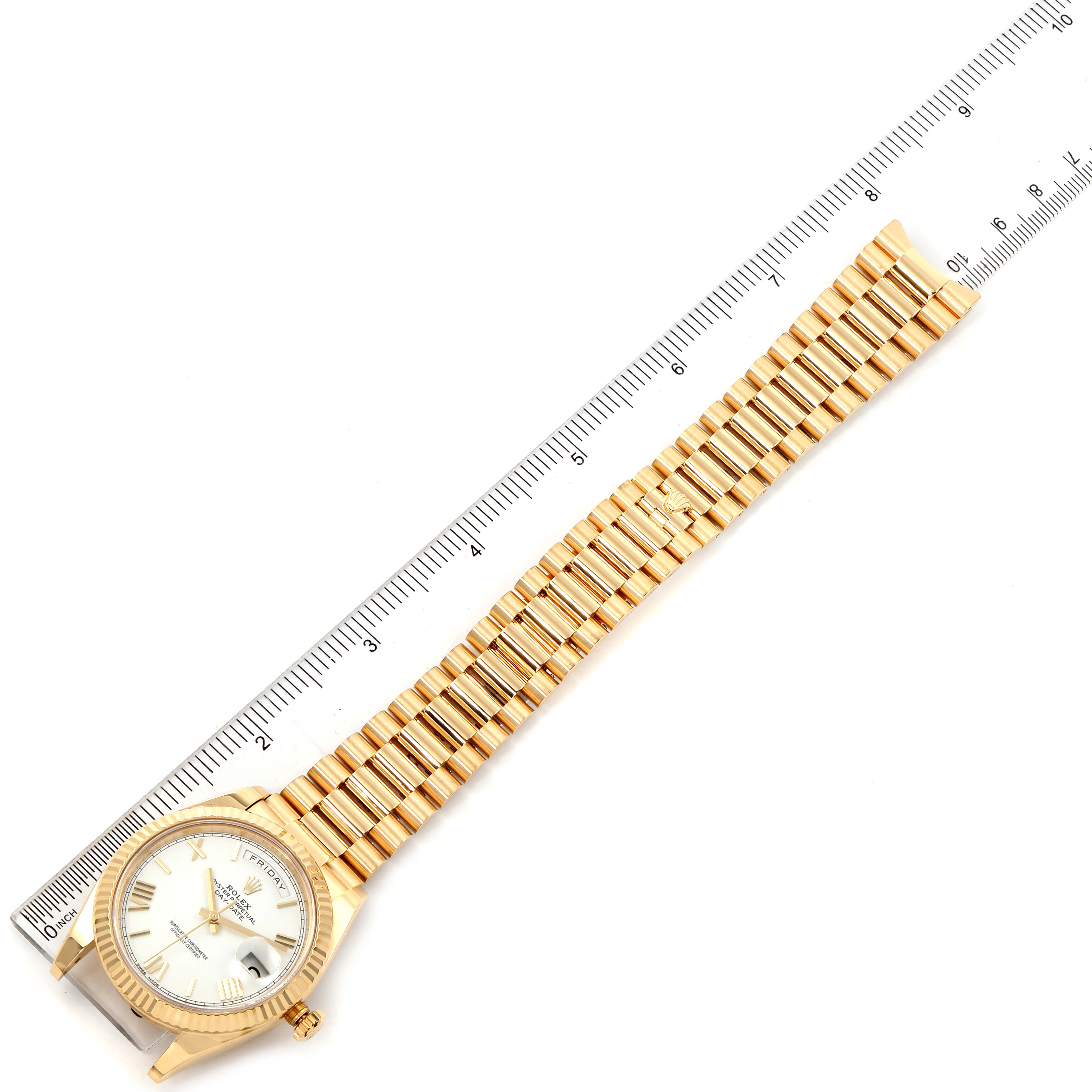 This image shows a President model Rolex watch laid next to a ruler, displaying its entire bracelet and dial.