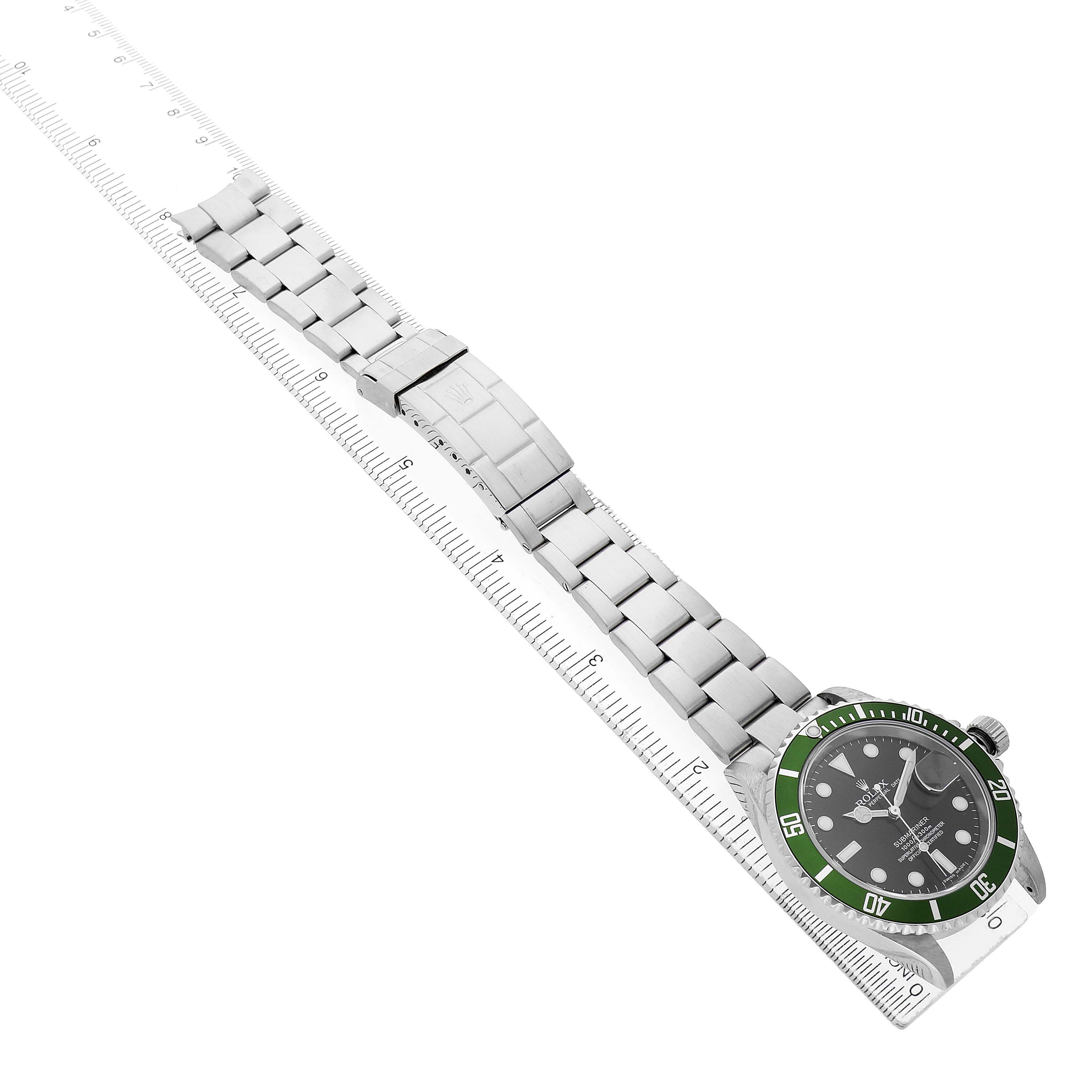 The Rolex Submariner 16610 Men's Stainless Steel Black Dial watch is shown at an oblique angle, displaying the green bezel, dial, and stainless steel bracelet alongside a ruler.