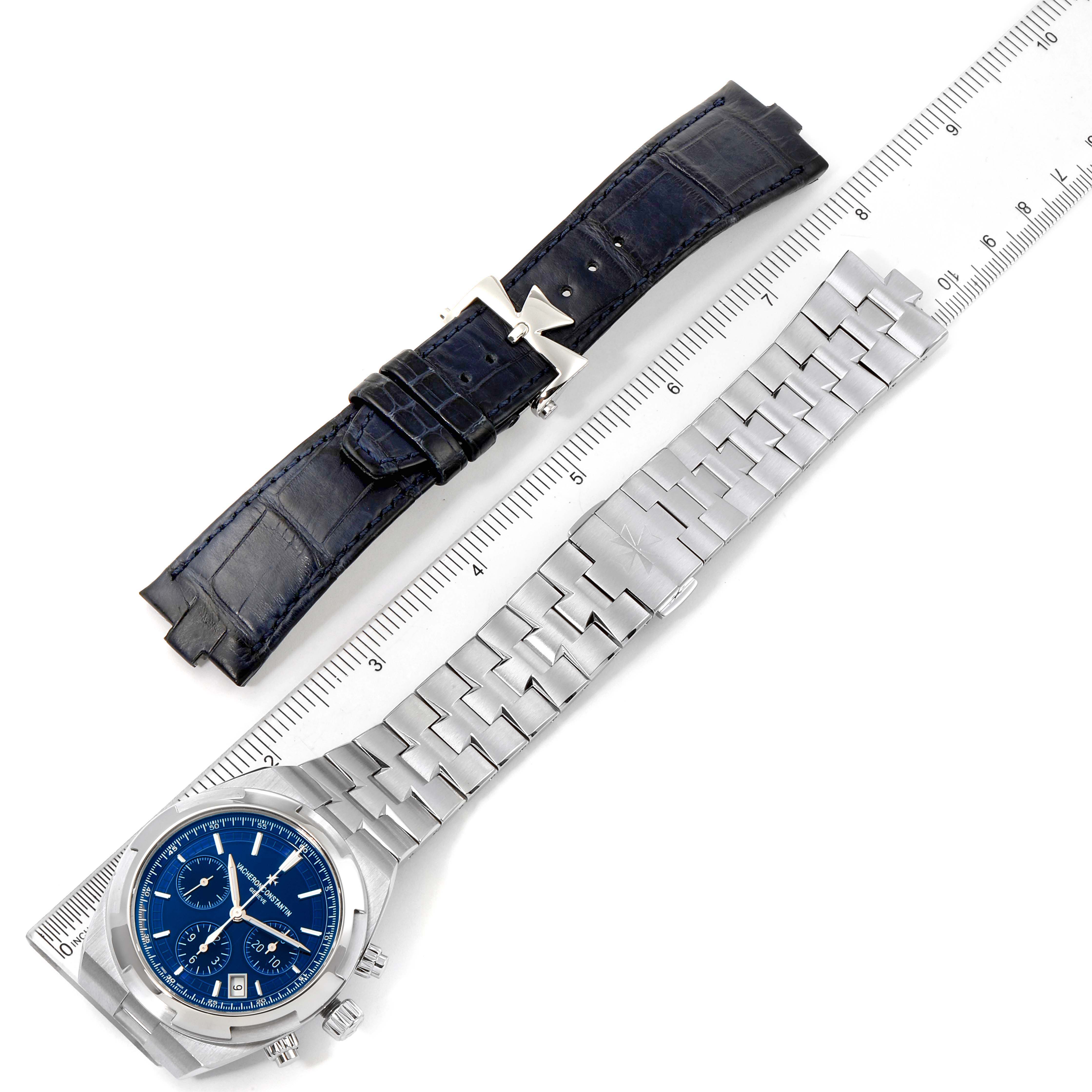 The image shows a Vacheron Constantin Overseas 5500V/110A-B148 Men's Stainless Steel Blue Dial 5500V/110A-B148 Men's Stainless Steel Blue Dial watch with a blue dial and an extra black leather strap laid out with a ruler.