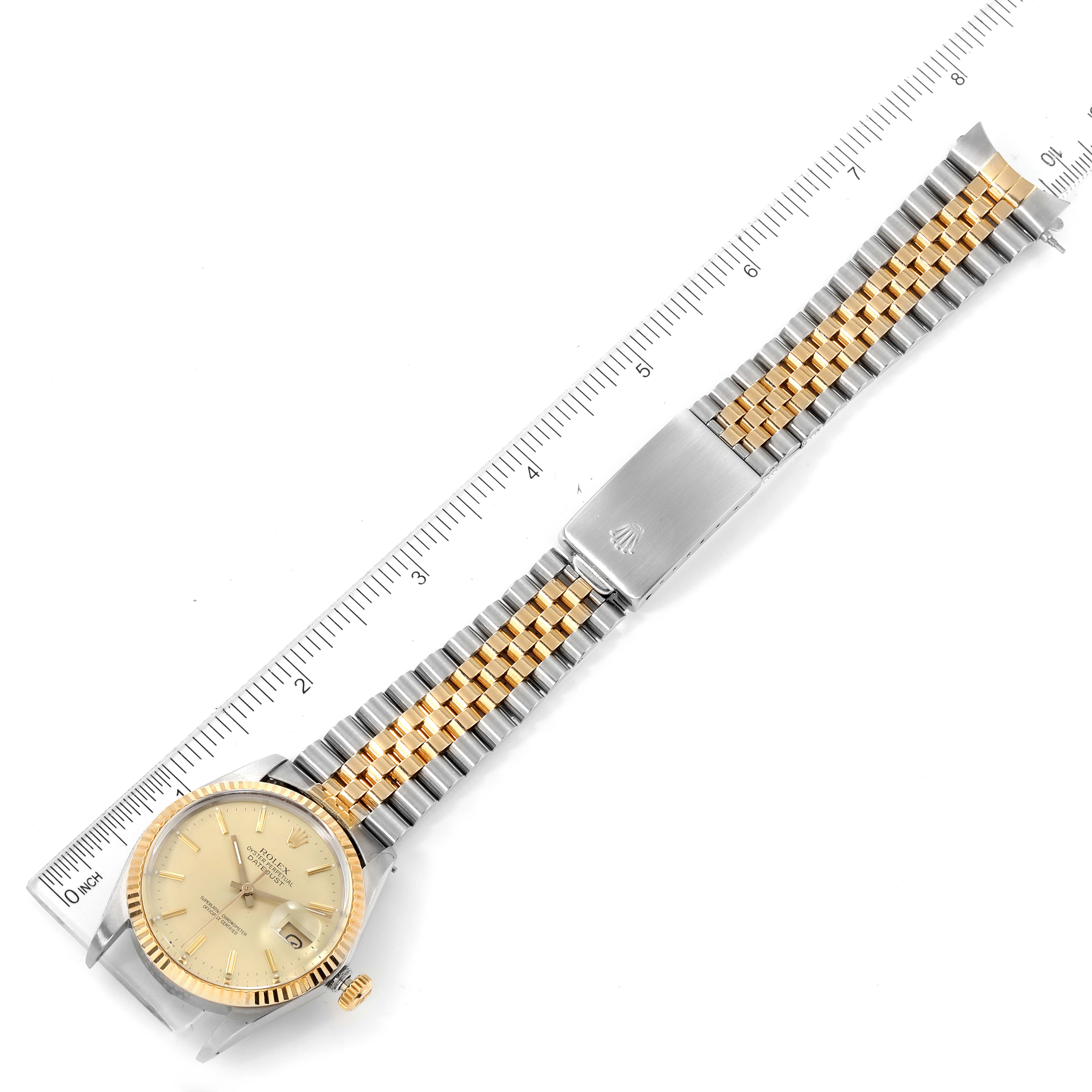 The image shows a top view of the Rolex Datejust 16013 Men's Steel and Gold (two tone) Champagne Dial 16013 Men's Steel and Gold (two tone) Champagne Dial watch with a gold and silver bracelet next to a ruler.