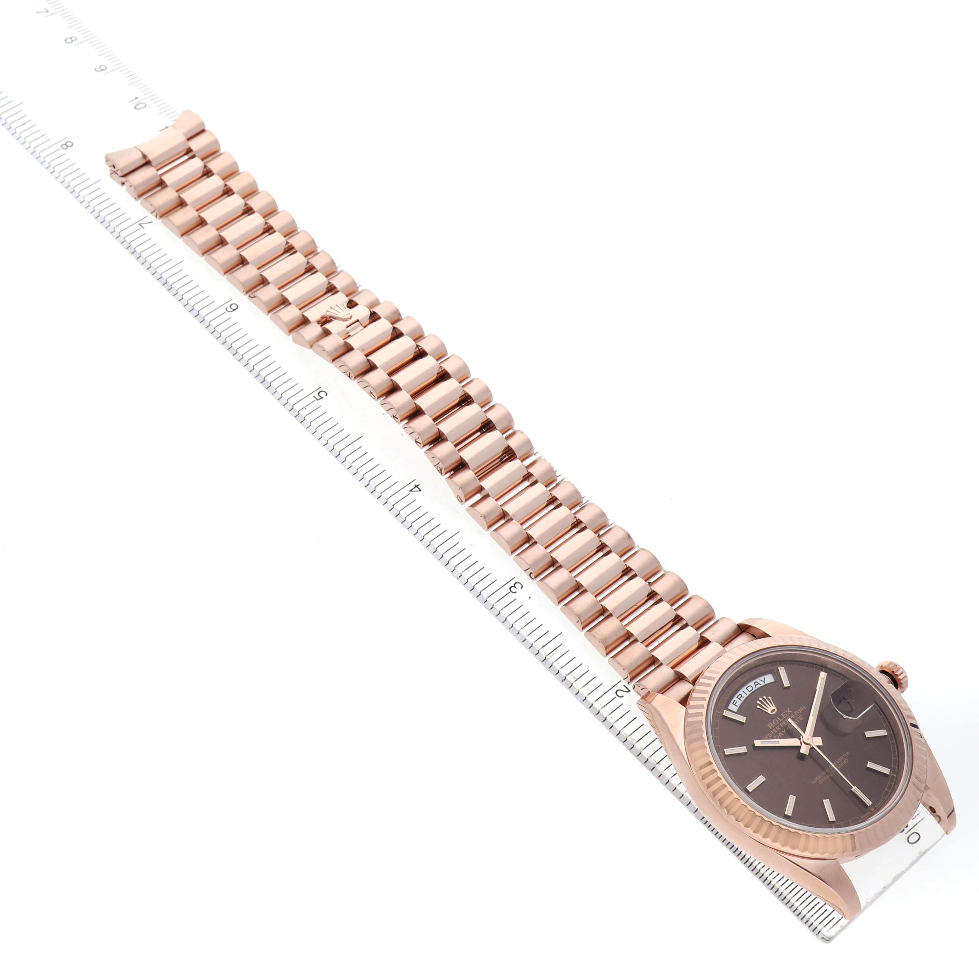 The Rolex President 228235 Men's Rose Gold Brown Dial watch is shown at an angle from the side, displaying the full bracelet and watch face alongside a ruler.