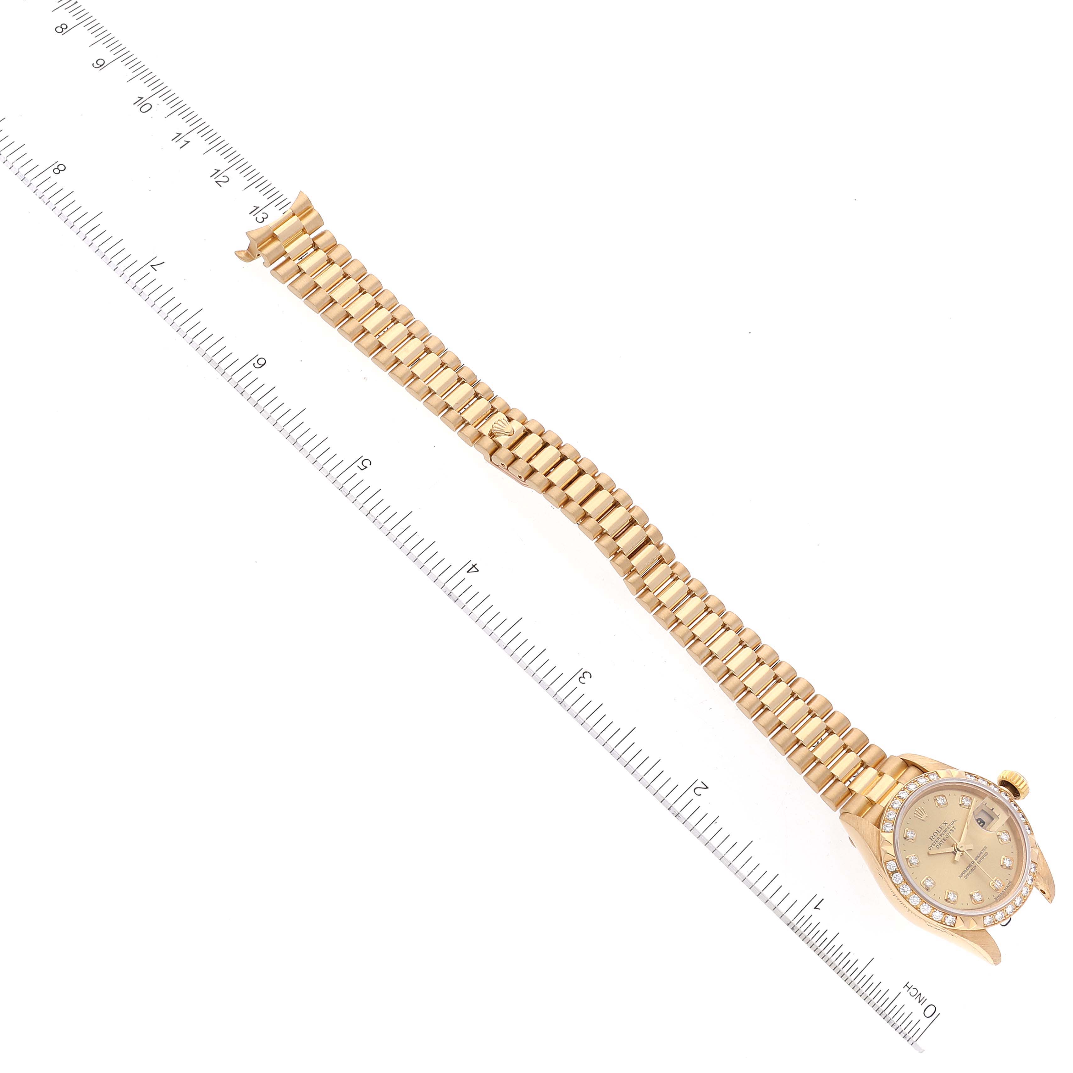 The image shows an overhead view of a Rolex President 79268 Women
s Yellow Gold Champagne Dial 79268 Women
s Yellow Gold Champagne Dial watch, displaying its full bracelet and part of the face along a ruler.