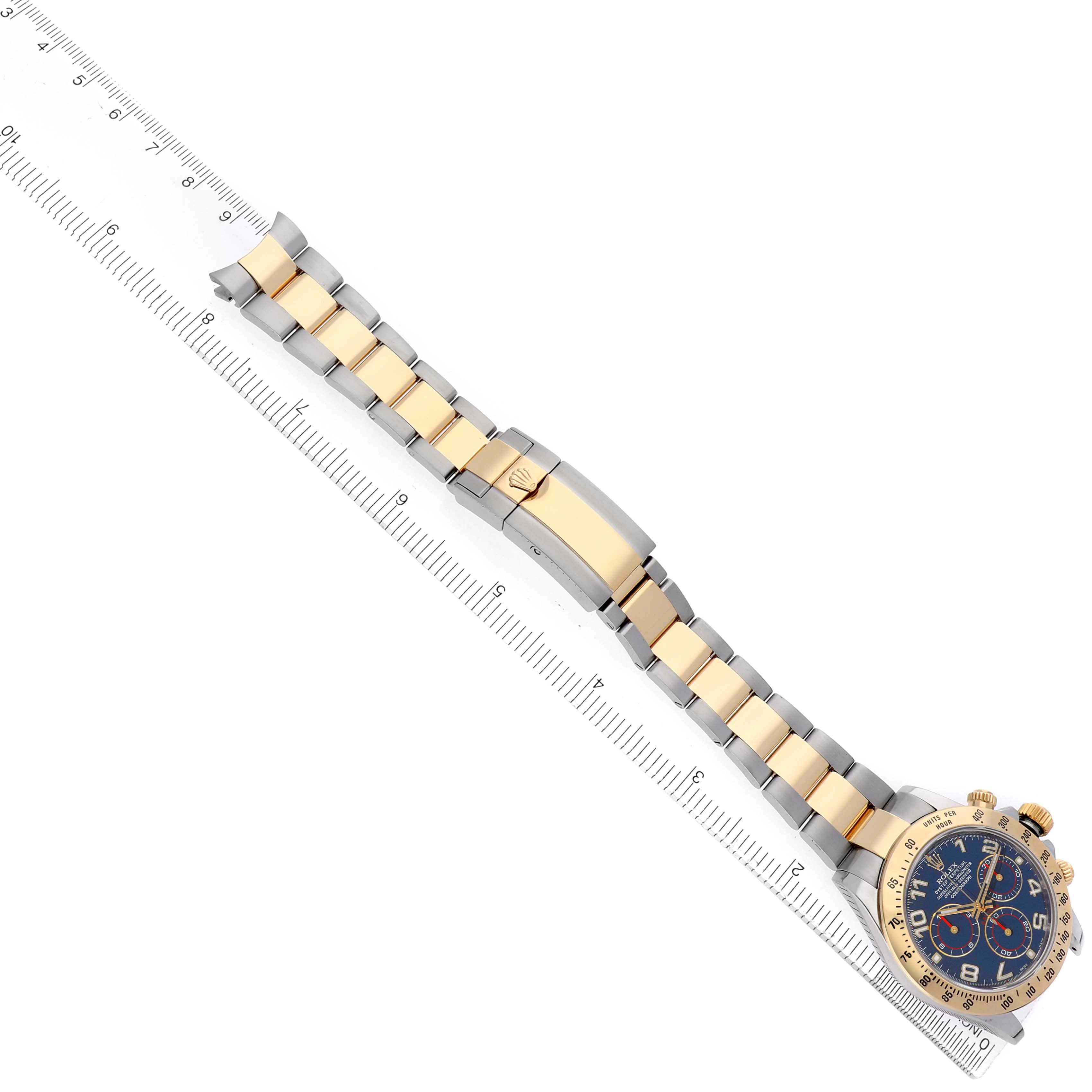 The image shows a top view of a Rolex Daytona 116523 Men's Steel and Gold (two tone) Blue Dial watch, highlighting its gold and silver bracelet, clasp, and face alongside a ruler.