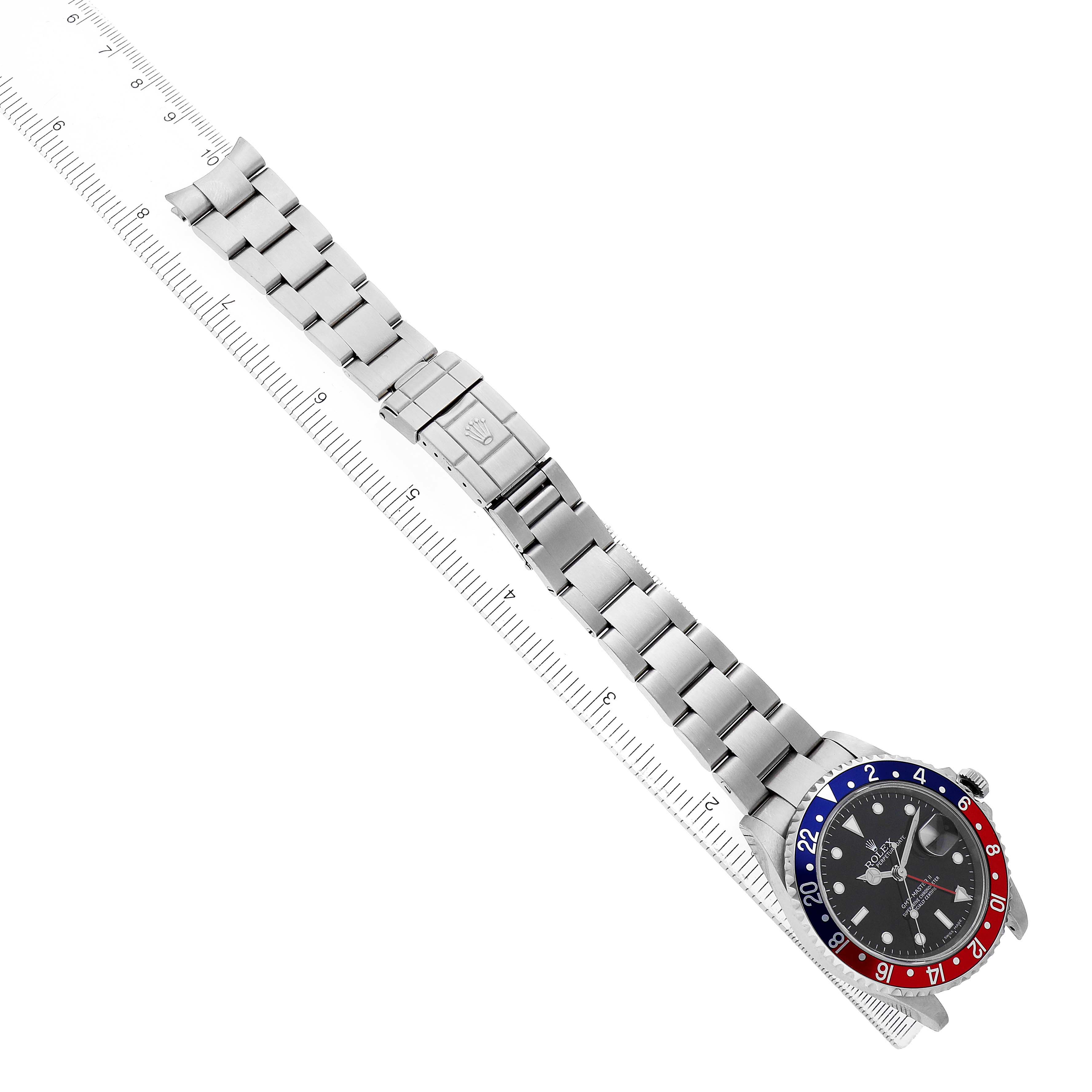 The Rolex GMT-Master 16710 Men's Stainless Steel Black Dial watch is shown from a top view, highlighting the bezel, dial, and bracelet fully extended alongside a ruler.