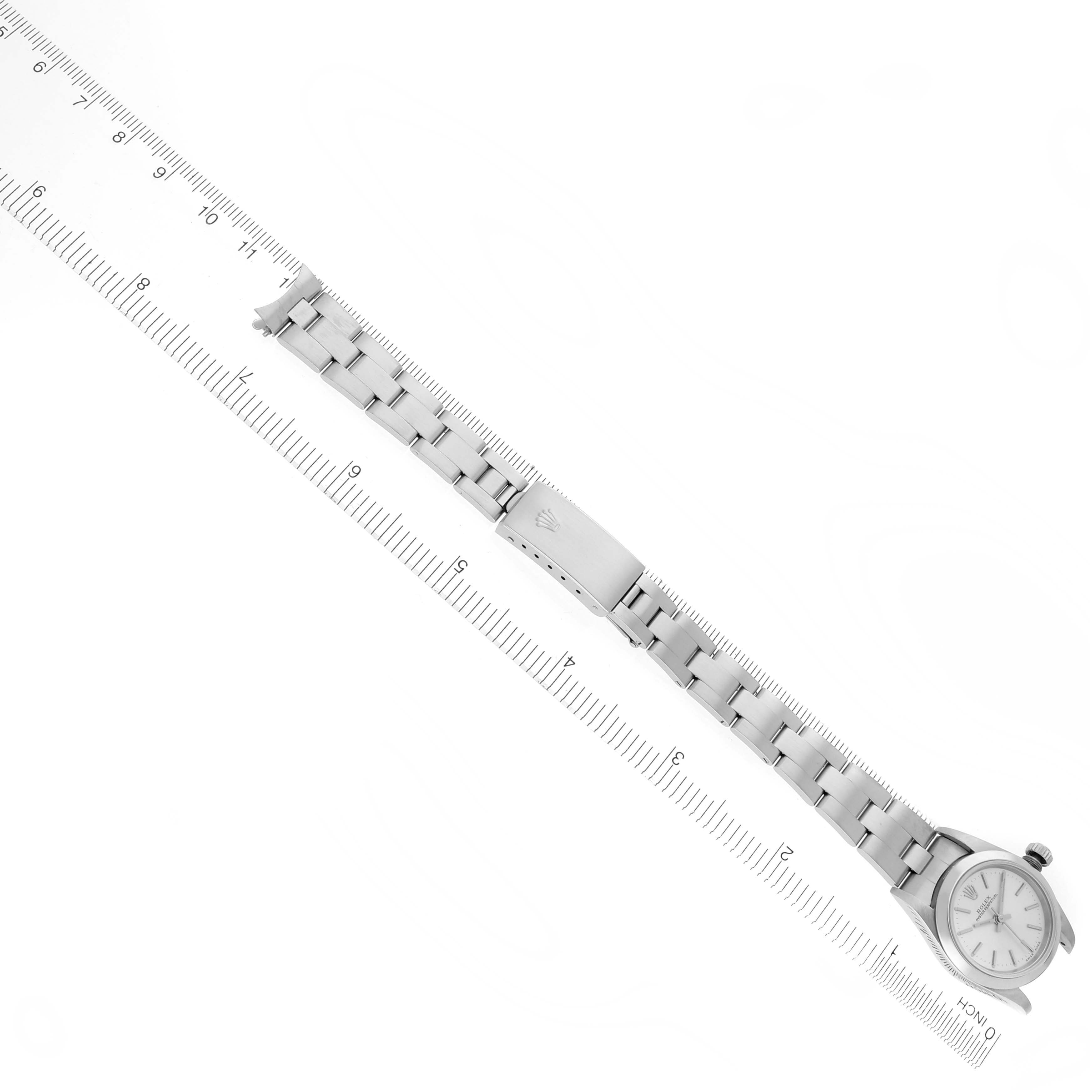 The Rolex Oyster Perpetual 76080 Women's Stainless Steel Silver Dial 76080 Women's Stainless Steel Silver Dial watch is shown at an angled top view, highlighting its bracelet and case alongside a ruler for scale.