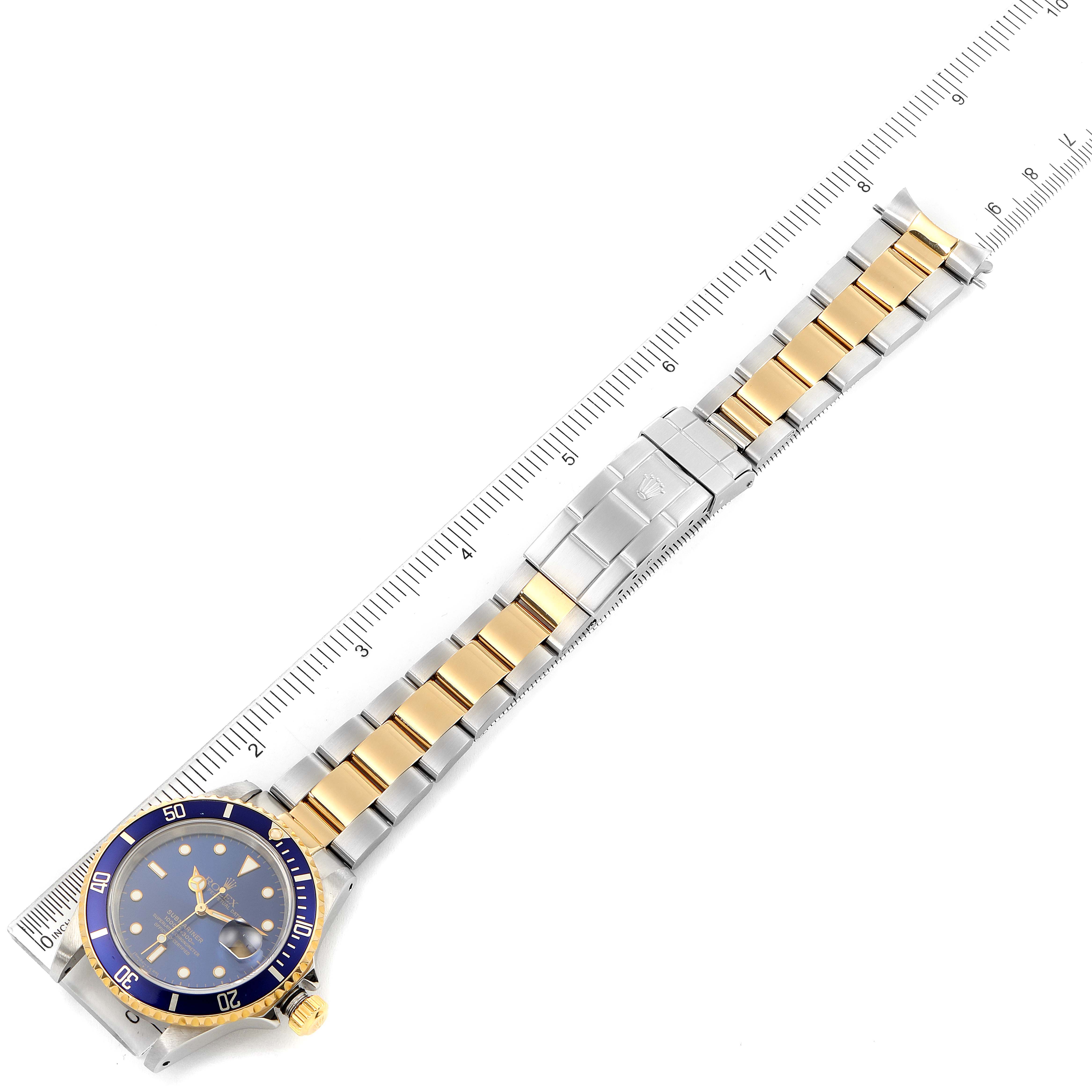 The Rolex Submariner 16613 Men
s Steel and Gold (two tone) Blue Dial 16613 Men
s Steel and Gold (two tone) Blue Dial watch is shown laid flat with the face and strap fully visible, alongside a measuring scale.
