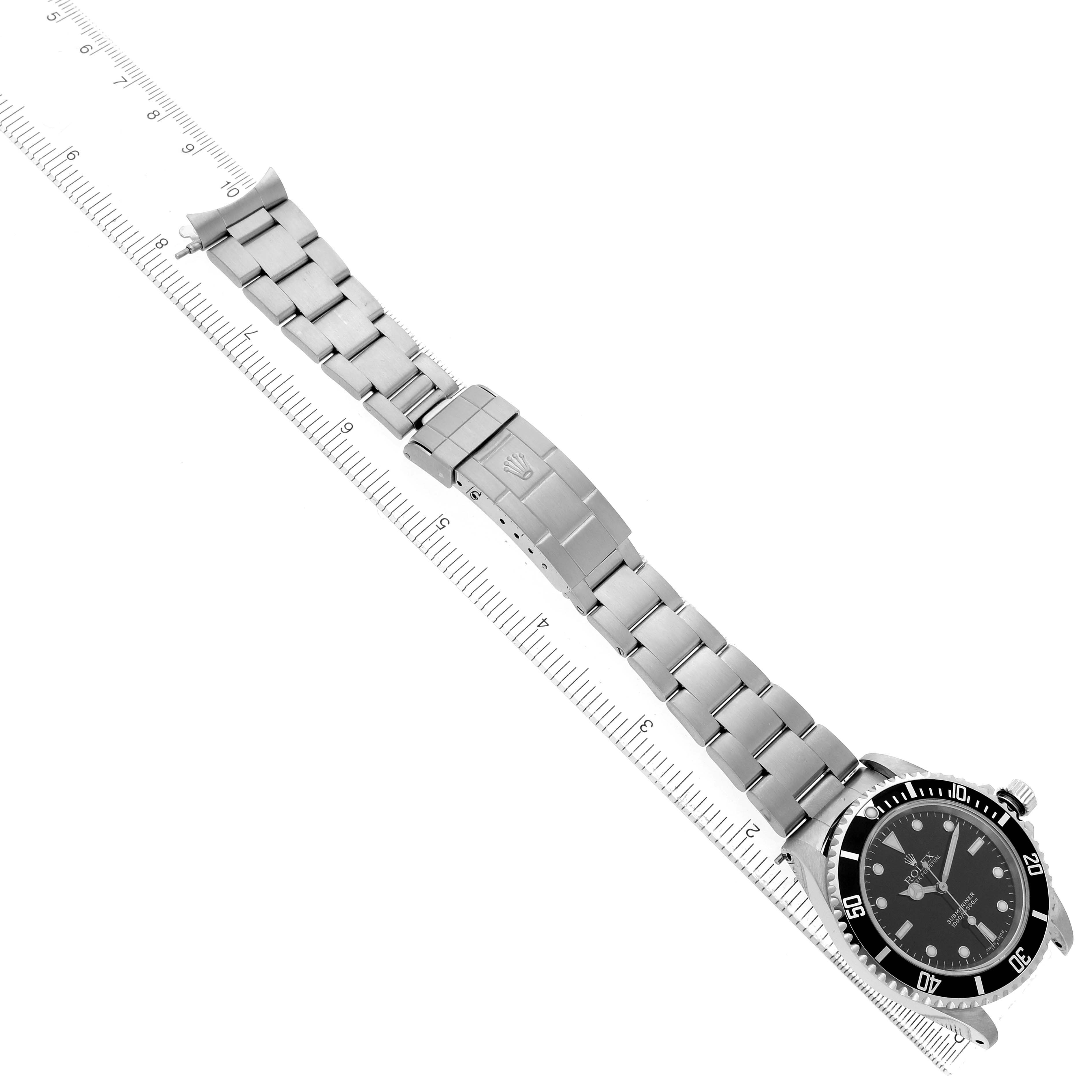 The Rolex Submariner 14060 Men's Stainless Steel Black Dial watch is shown from a top angle, displaying the face, bracelet, and clasp aligned with a ruler.