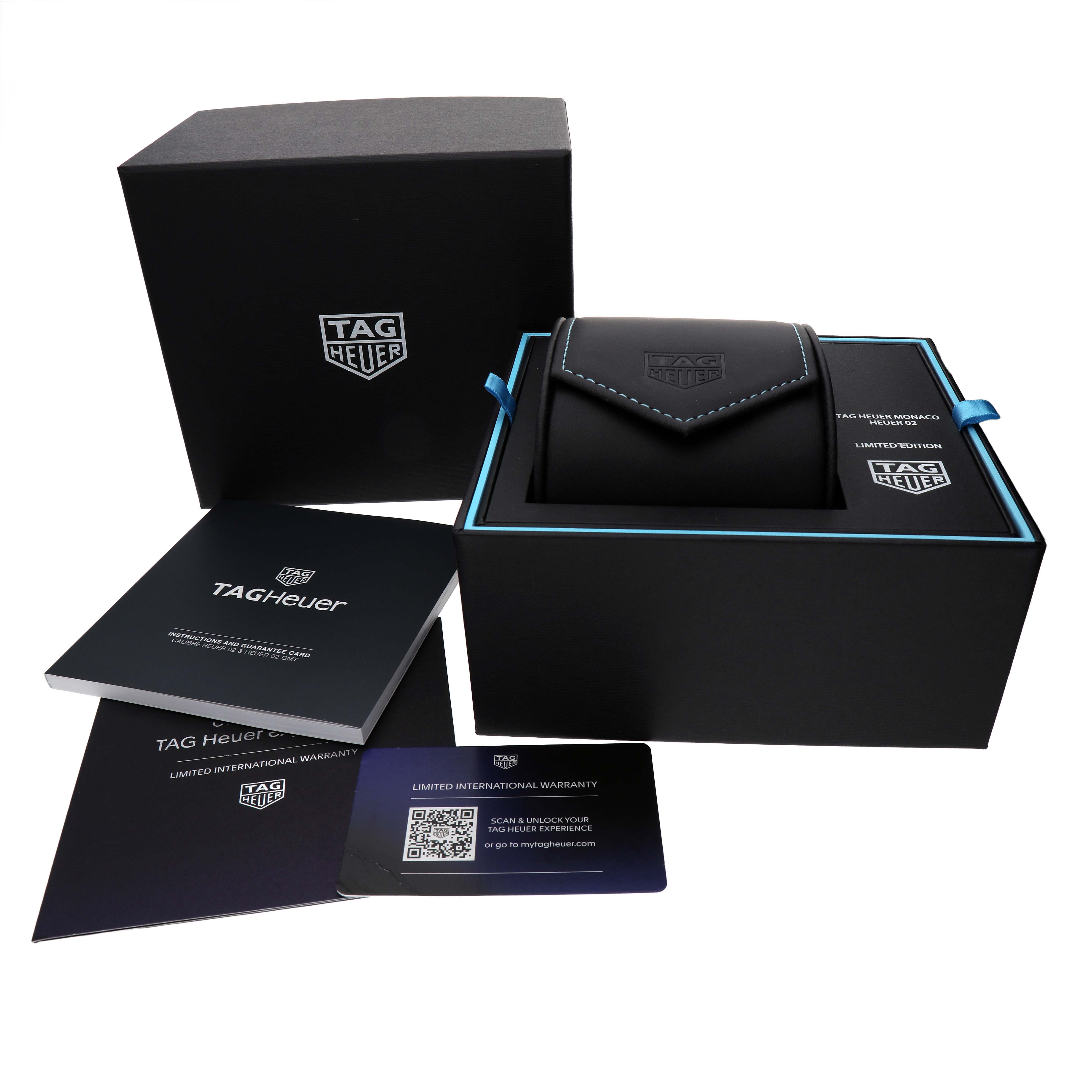 The image shows a TAG Heuer Monaco watch box set with packaging, a carrying case, manuals, and a warranty card.