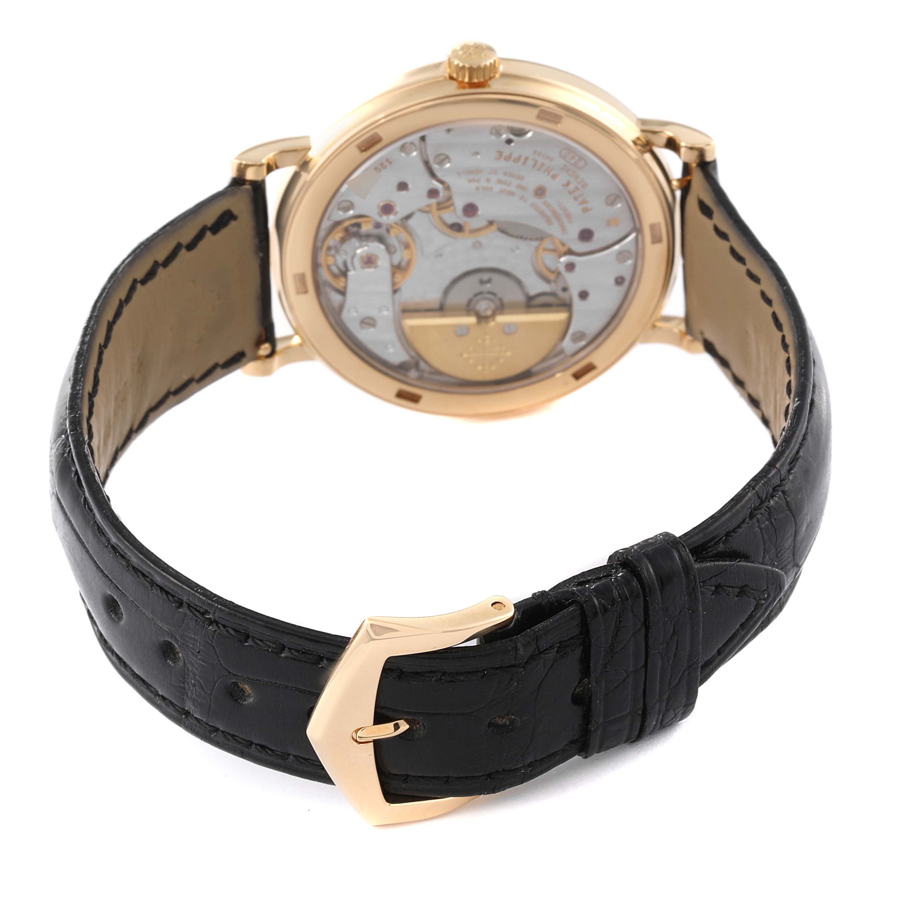 The image shows the back view of the Patek Philippe Calatrava 5120J Men's Yellow Gold White Dial 5120J Men's Yellow Gold White Dial watch, highlighting its movement and black leather strap with a buckle.
