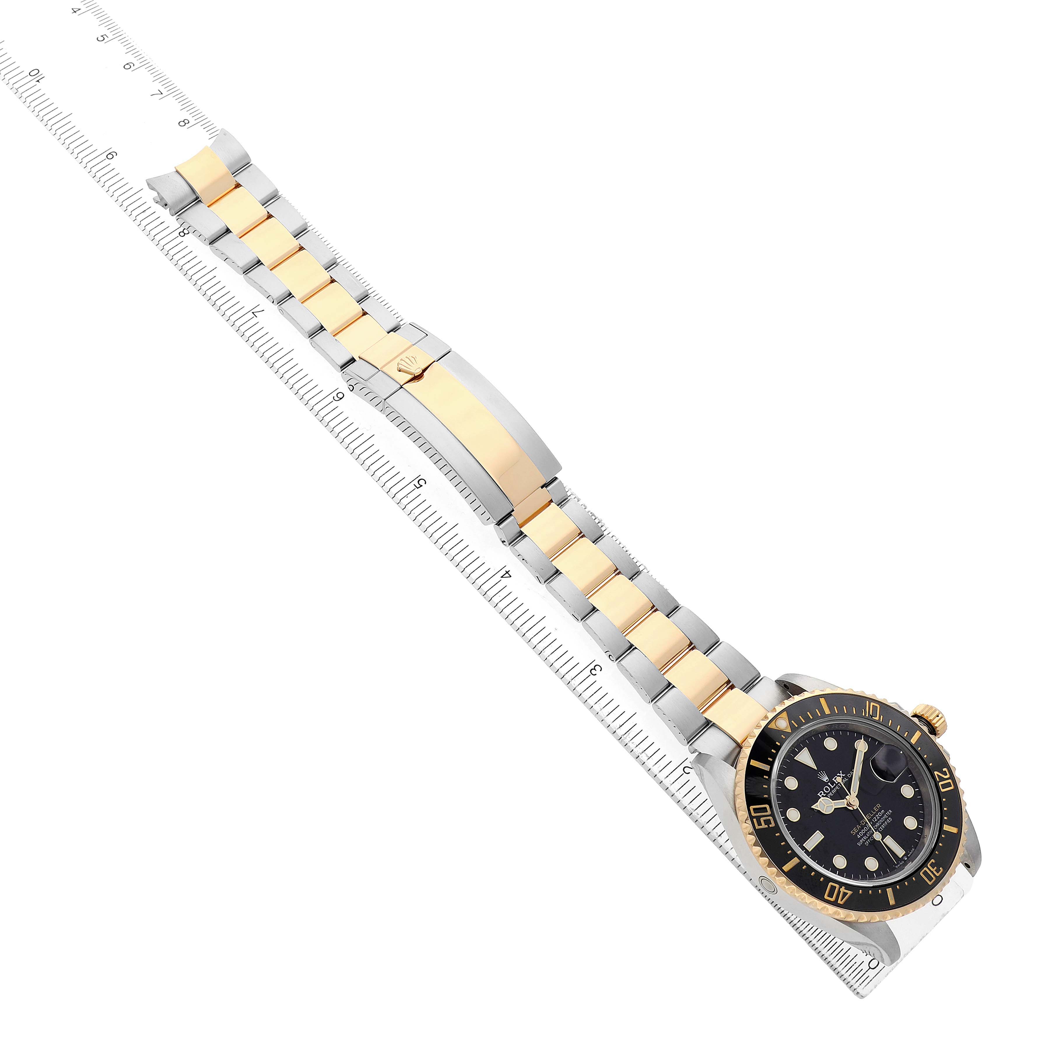 The Rolex Sea-Dweller 126603 Men's Steel and Gold (two tone) Black Dial watch is shown at an angled top view, featuring the bracelet and bezel on a ruler.