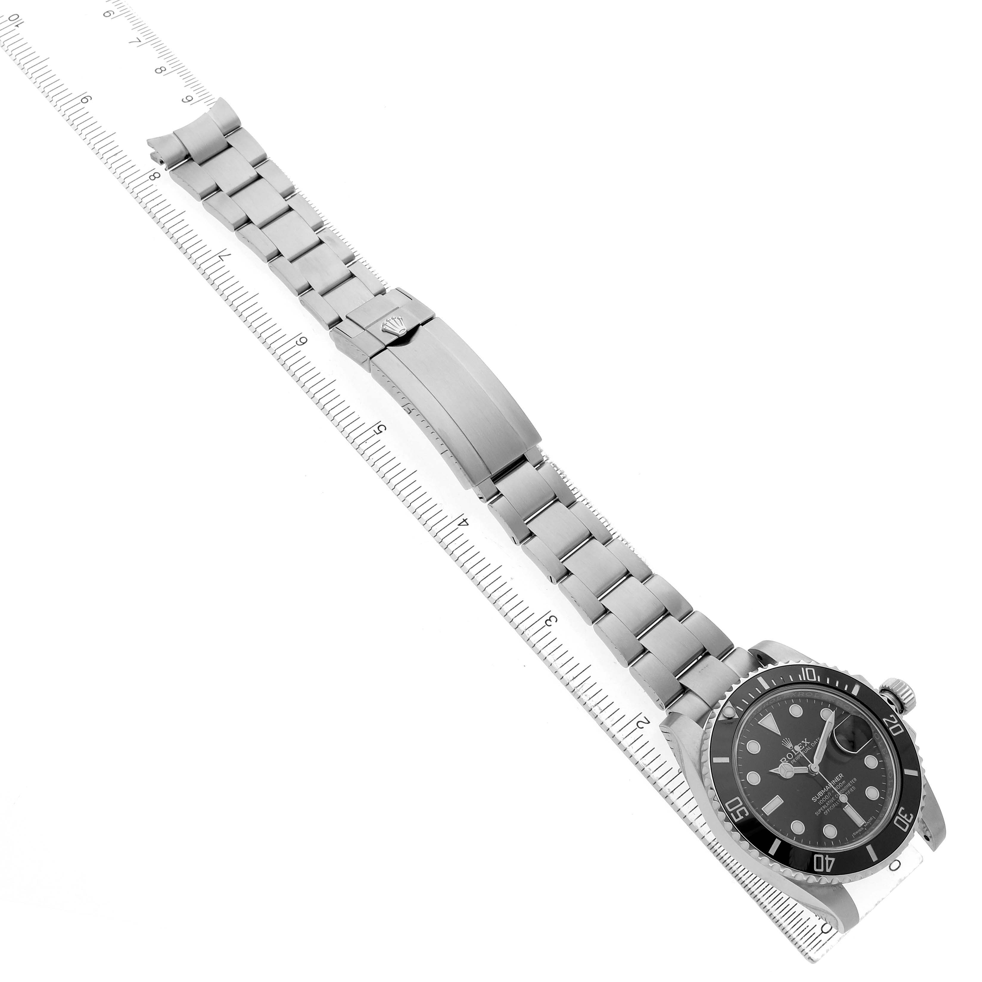 The Rolex Submariner 116610 Men's Stainless Steel Black Dial watch is shown at an angled view, displaying the face, bezel, and bracelet alongside a ruler.