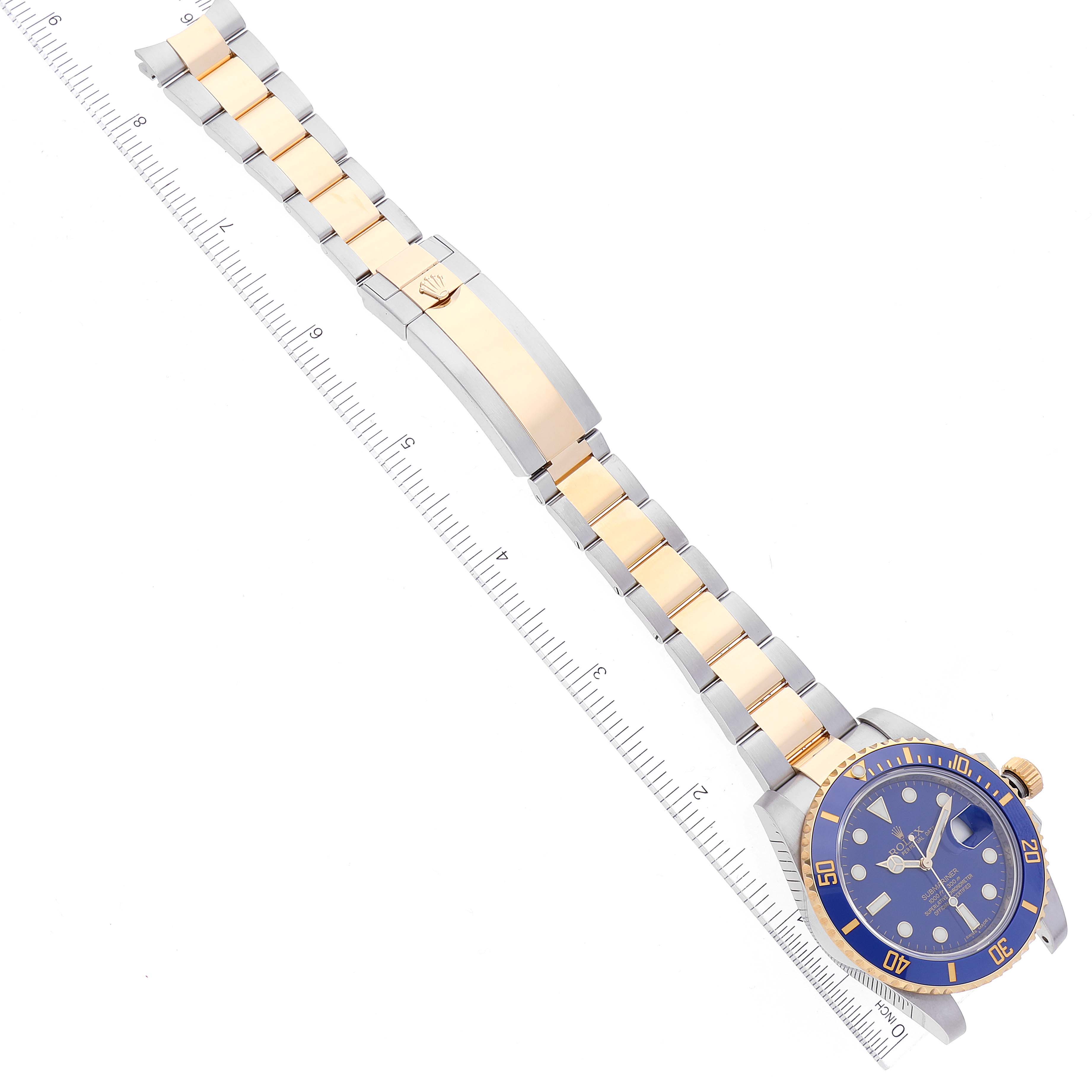The image shows a Rolex Submariner 116613 Men's Steel and Gold (two tone) Blue Dial 116613 Men's Steel and Gold (two tone) Blue Dial watch viewed from above, displaying the face, bezel, and full band extended next to a ruler.