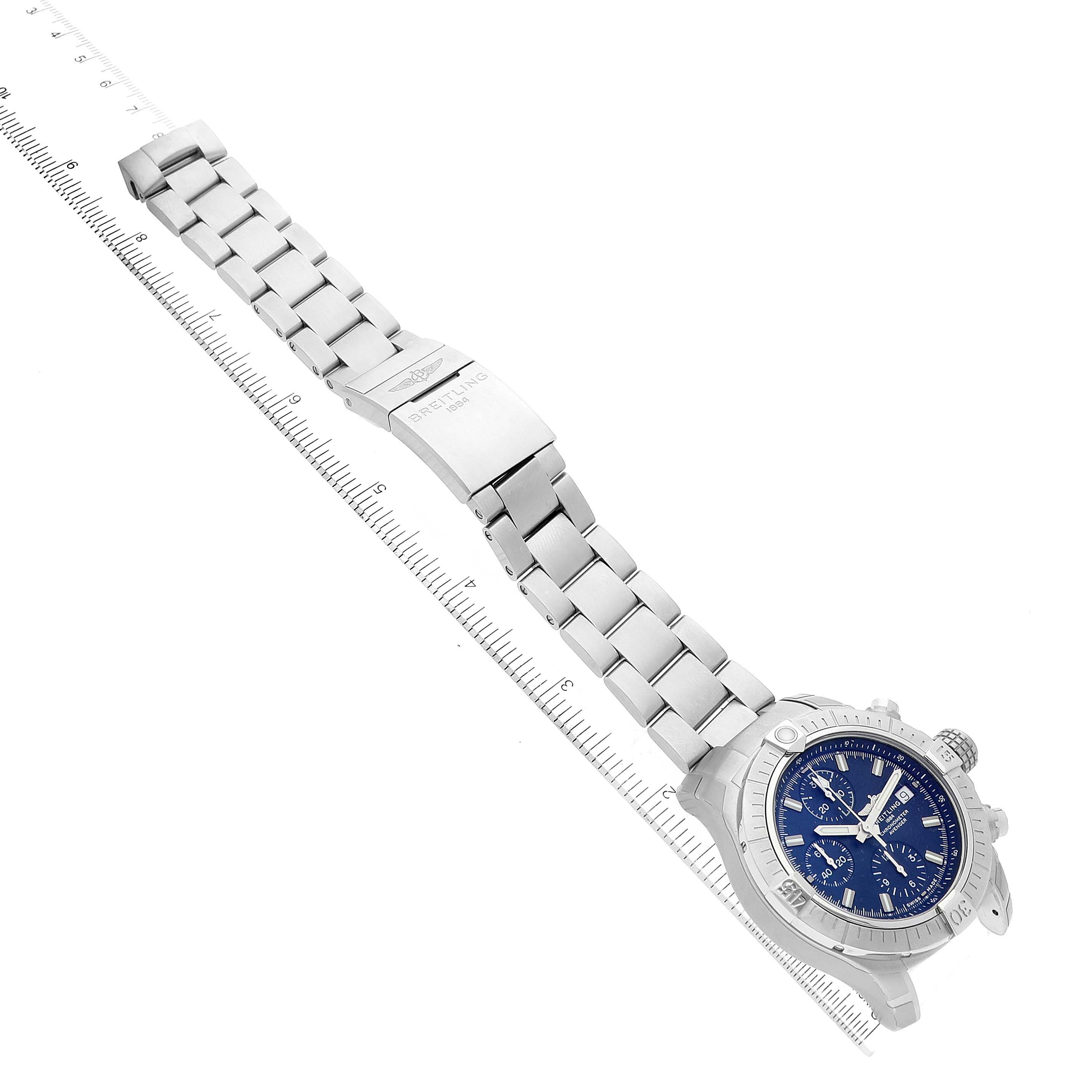 The image shows a top-down view of a Breitling Avenger A13385 Men's Stainless Steel Blue Dial A13385 Men's Stainless Steel Blue Dial watch, featuring its blue dial, stainless steel case, and bracelet against a ruler.