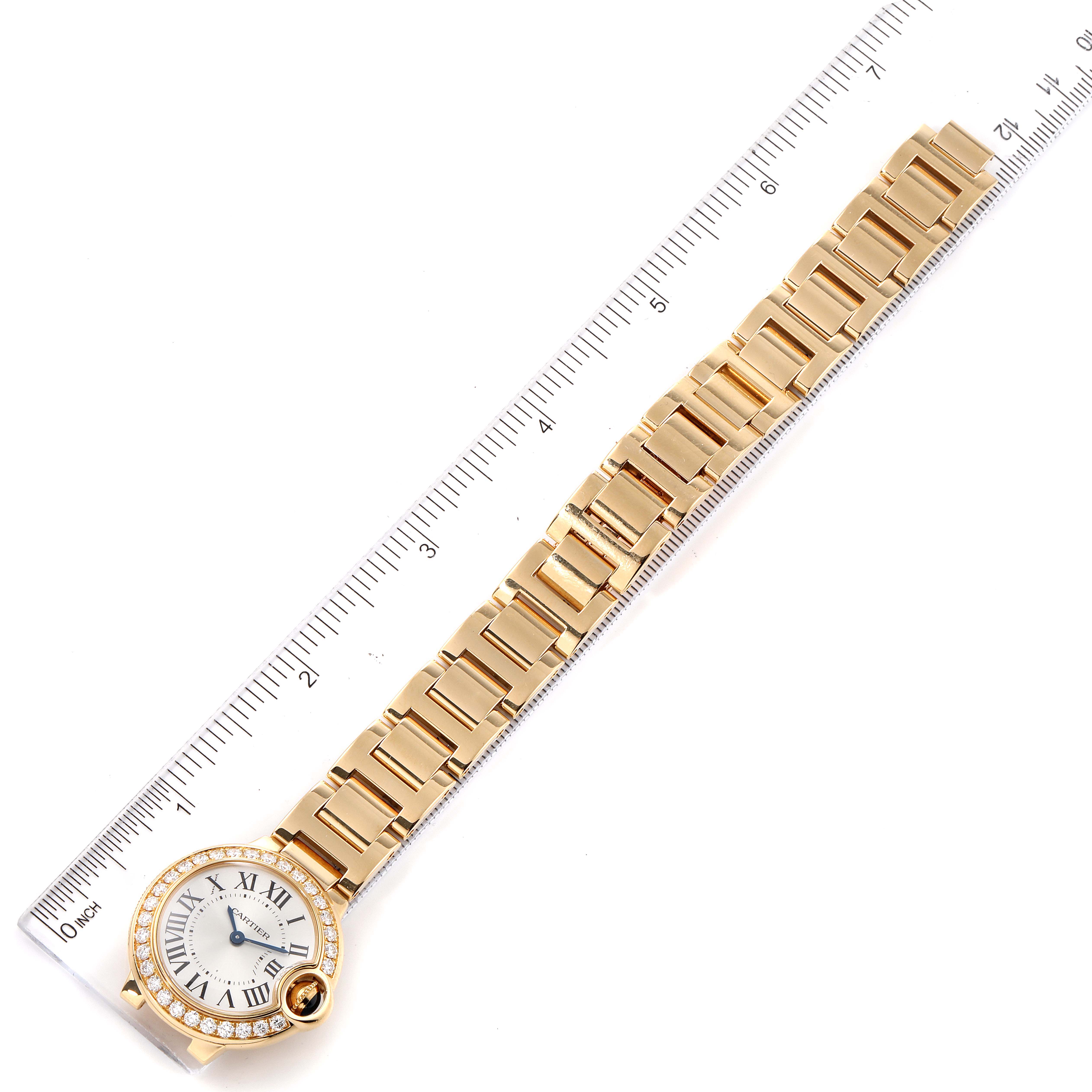 The image shows the full view of a Cartier Ballon Bleu WE9001Z3 Women's Yellow Gold Silver Dial WE9001Z3 Women's Yellow Gold Silver Dial model watch, including its face and gold bracelet, placed against a ruler for scale.