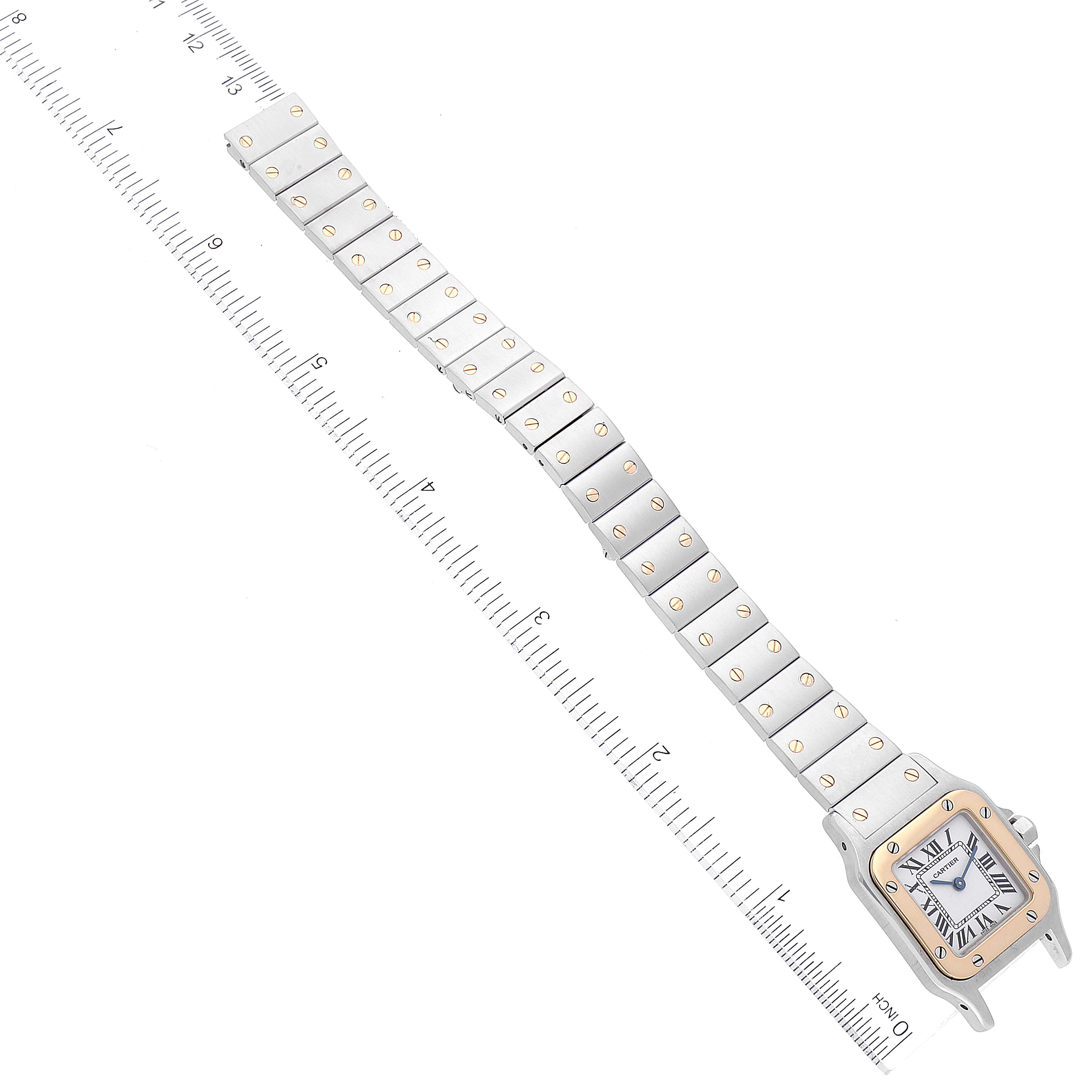 The image shows a top view of the Santos model by Cartier, including its watch face and full metal bracelet, alongside a ruler for scale.