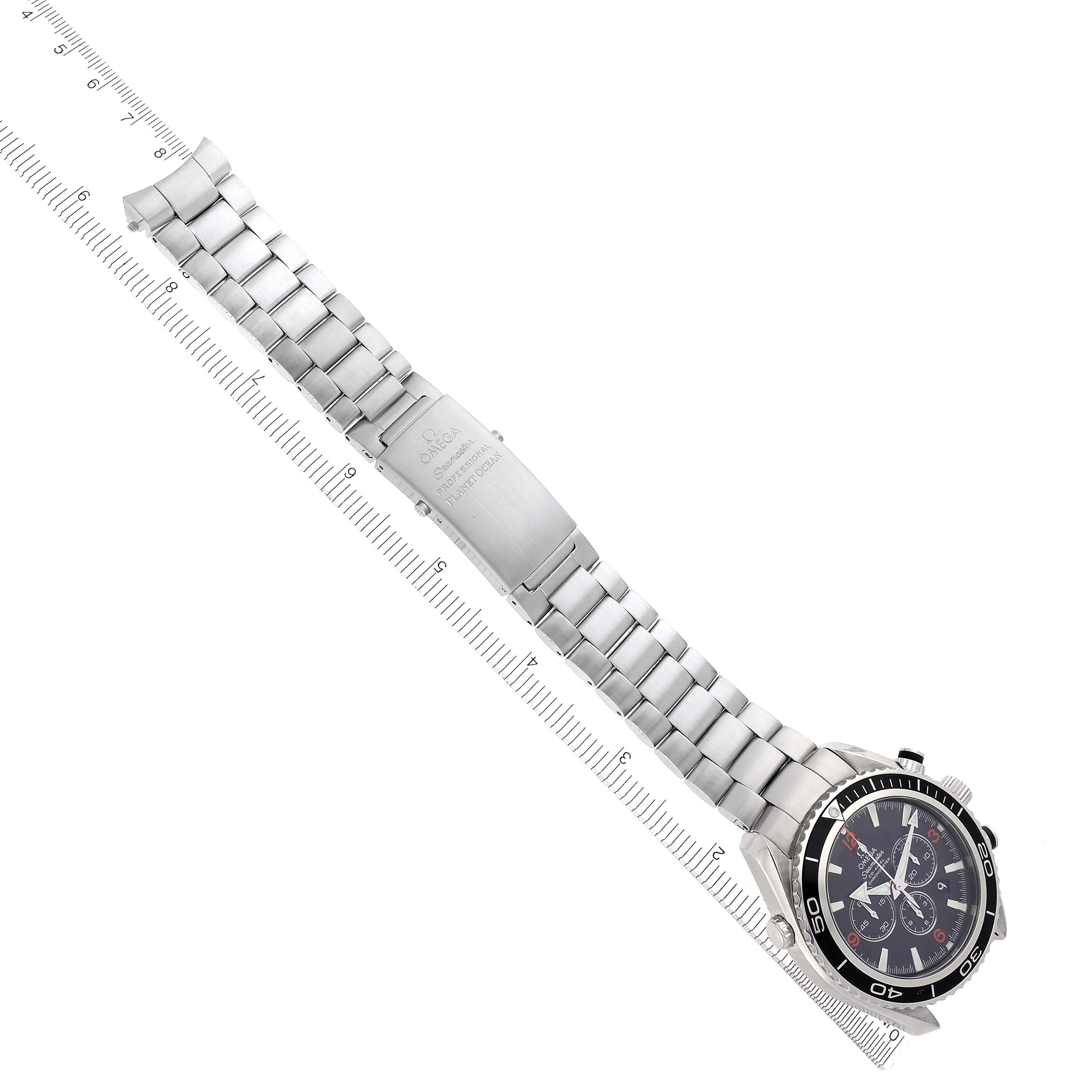 The Omega Planet Ocean 2210.51.00 Men's Stainless Steel Black Dial 2210.51.00 Men's Stainless Steel Black Dial watch is shown from a top angle, displaying the bracelet, clasp, and watch face aligned with a ruler.