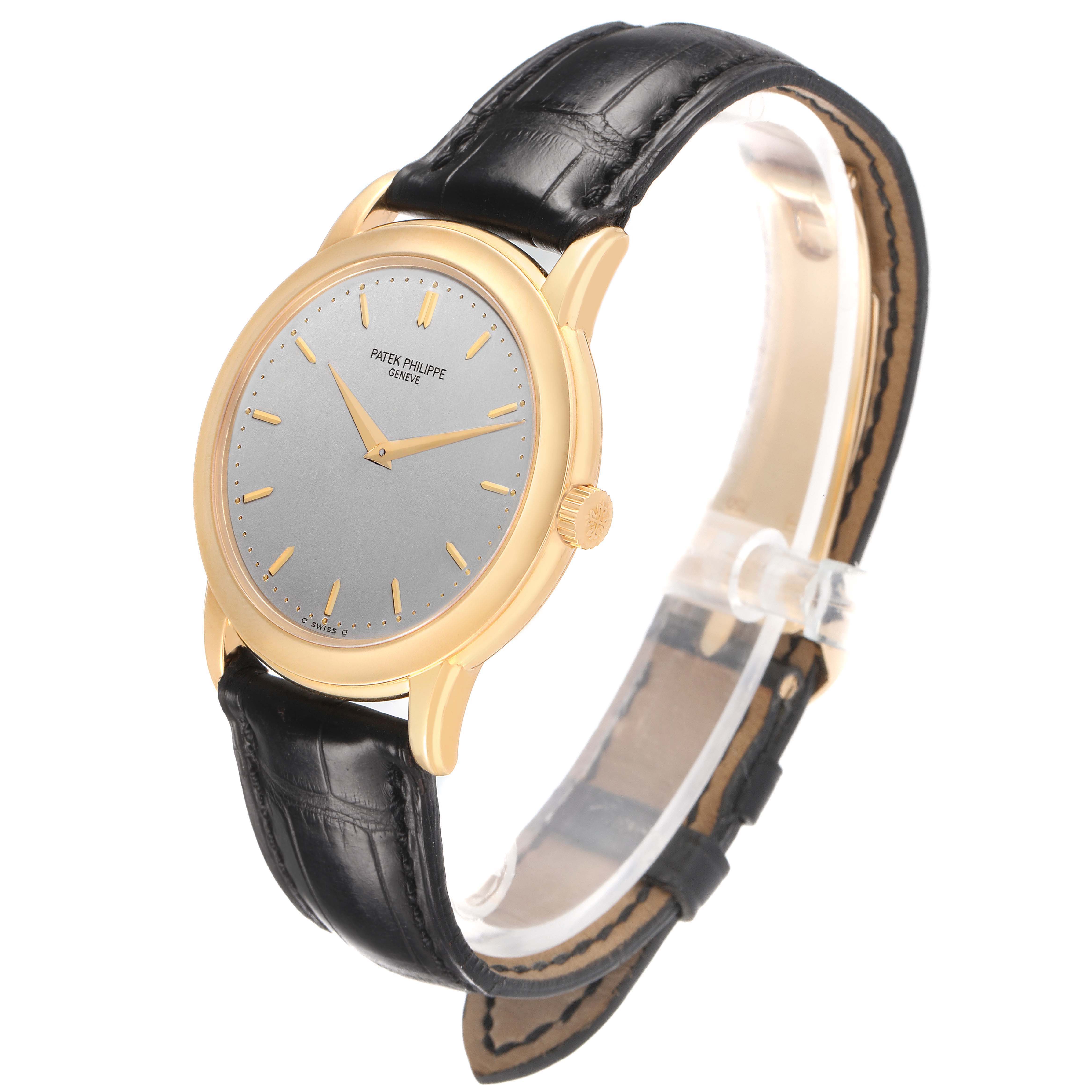 The Patek Philippe Calatrava 5032J Men's Yellow Gold Silver Dial watch is viewed at a three-quarter angle, showing its gold case, grey dial, and black leather strap.