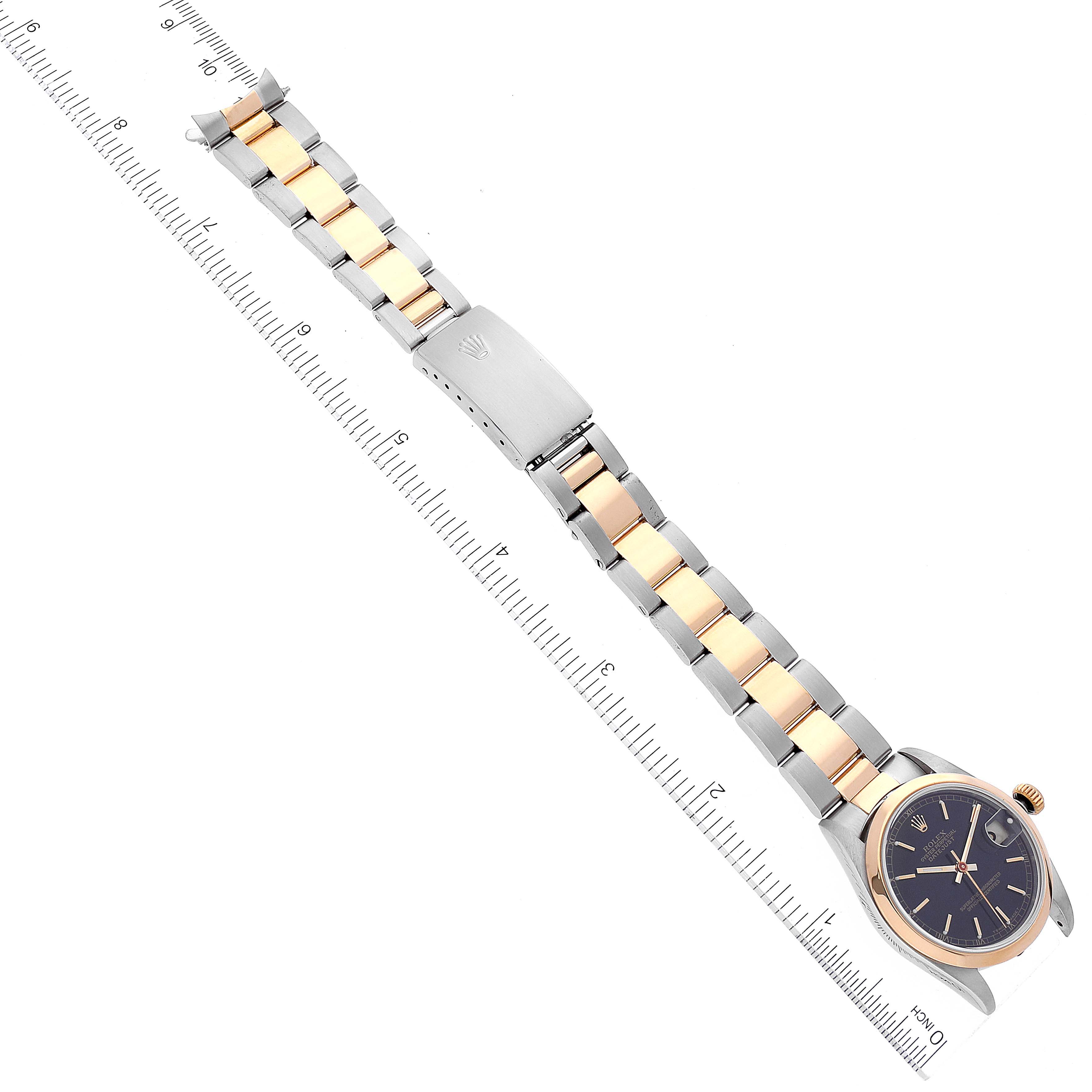 The image shows a Rolex Mid-Size 68243 Women
s Steel and Gold (two tone) Black Dial 68243 Women
s Steel and Gold (two tone) Black Dial watch at an aerial angle with its face, bezel, and two-tone bracelet visible alongside a ruler.