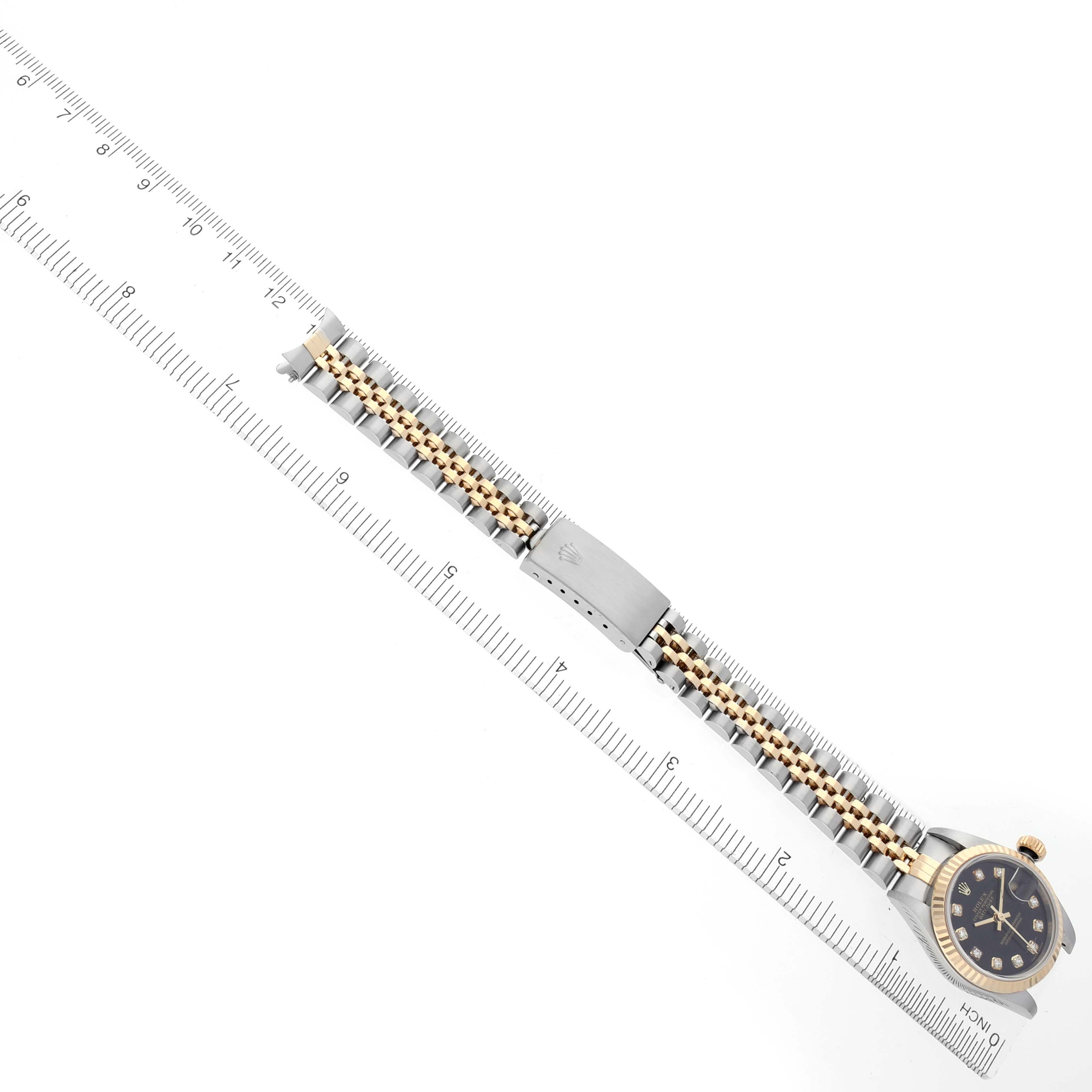 The Rolex Datejust 79173 Women's Steel and Gold (two tone) Black Dial 79173 Women's Steel and Gold (two tone) Black Dial is shown from a top view, featuring the watch face, bracelet, and clasp alongside a ruler for scale.