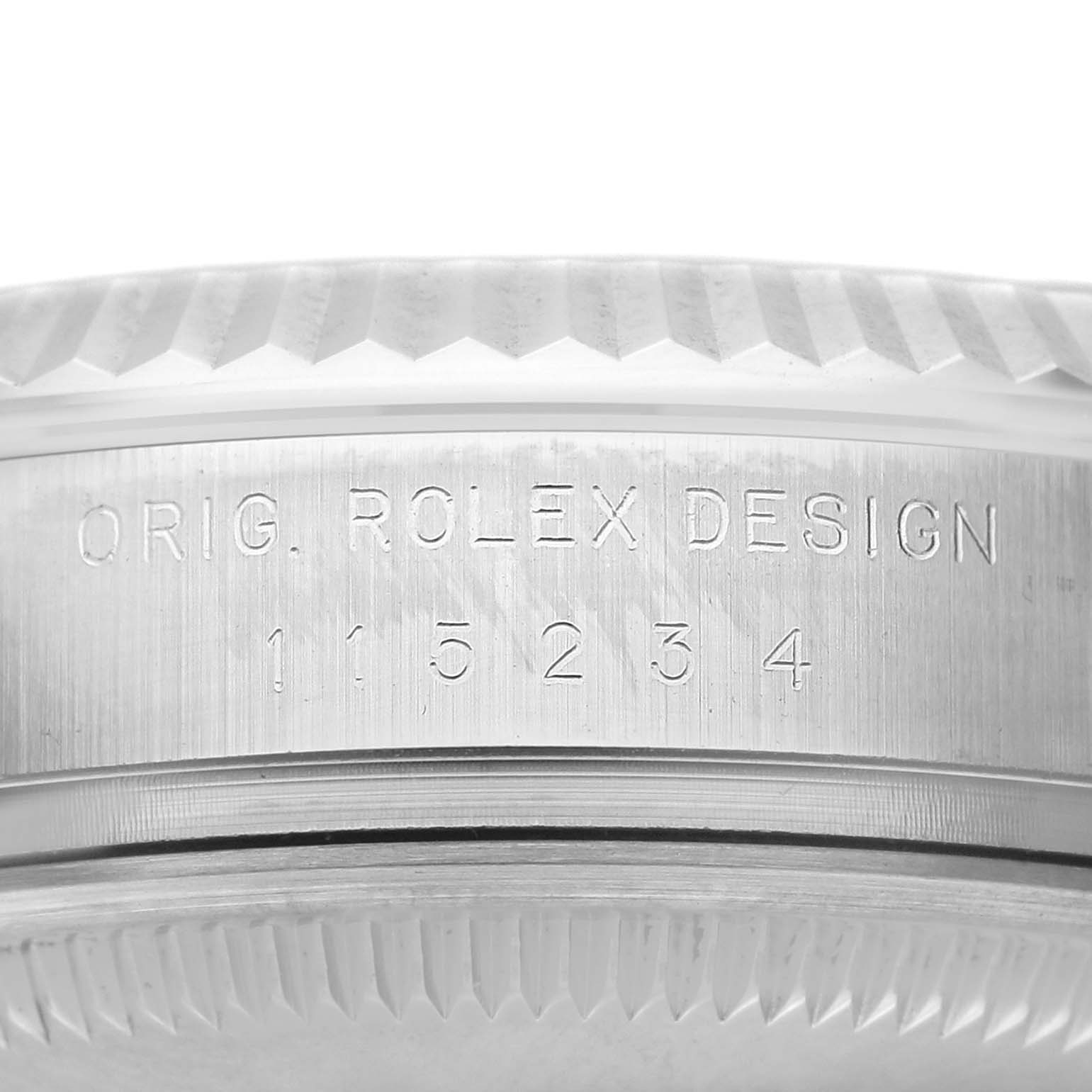 The image shows a close-up of the side of a Rolex Date 115234 Men's Stainless Steel Black Dial 115234 Men's Stainless Steel Black Dial watch case, featuring the model number "115234" and "ORIG. ROLEX DESIGN" engraving.