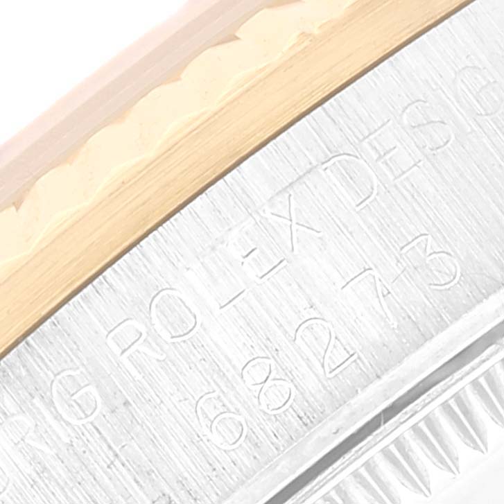 This close-up image of the Rolex Mid-Size 68273 Women
s Steel and Gold (two tone) Silver Dial 68273 Women
s Steel and Gold (two tone) Silver Dial model shows part of the watch case with engraved text and the edge of the bezel.