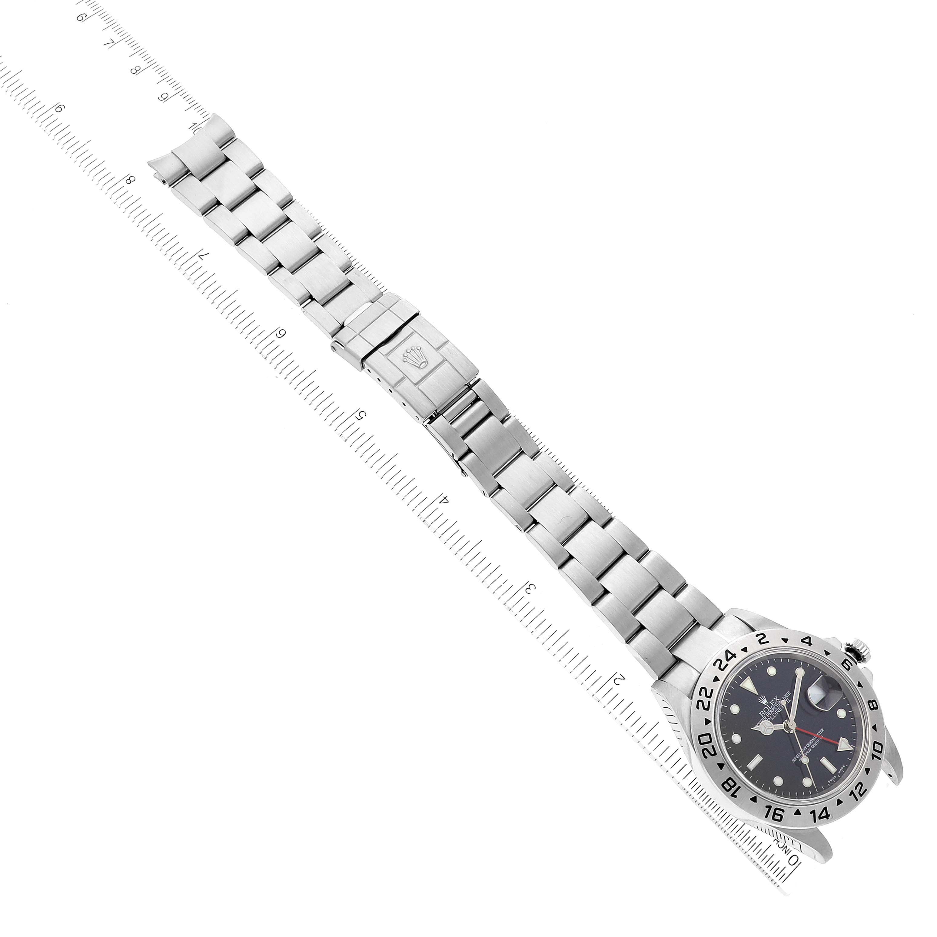 The image shows a top-down view of a Rolex Explorer 16570 Men's Stainless Steel Black Dial 16570 Men's Stainless Steel Black Dial model watch with its metal bracelet fully extended alongside a ruler.