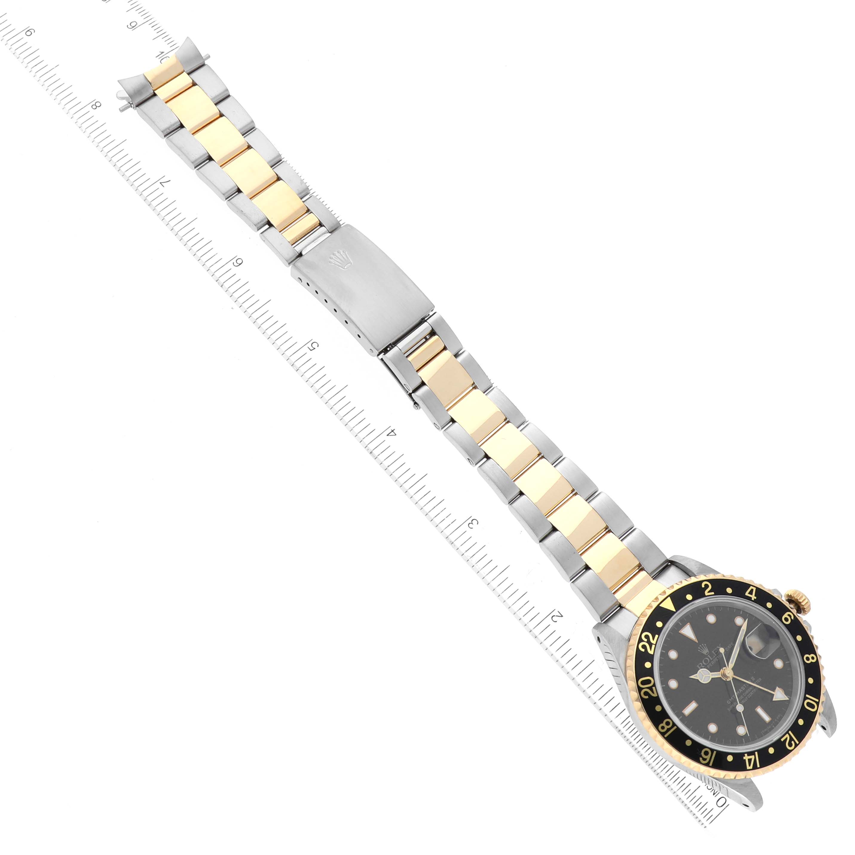 The image shows a top-down view of a Rolex GMT-Master 16713 Men's Steel and Gold (two tone) Black Dial 16713 Men's Steel and Gold (two tone) Black Dial watch with its bracelet extended alongside a ruler for scale.