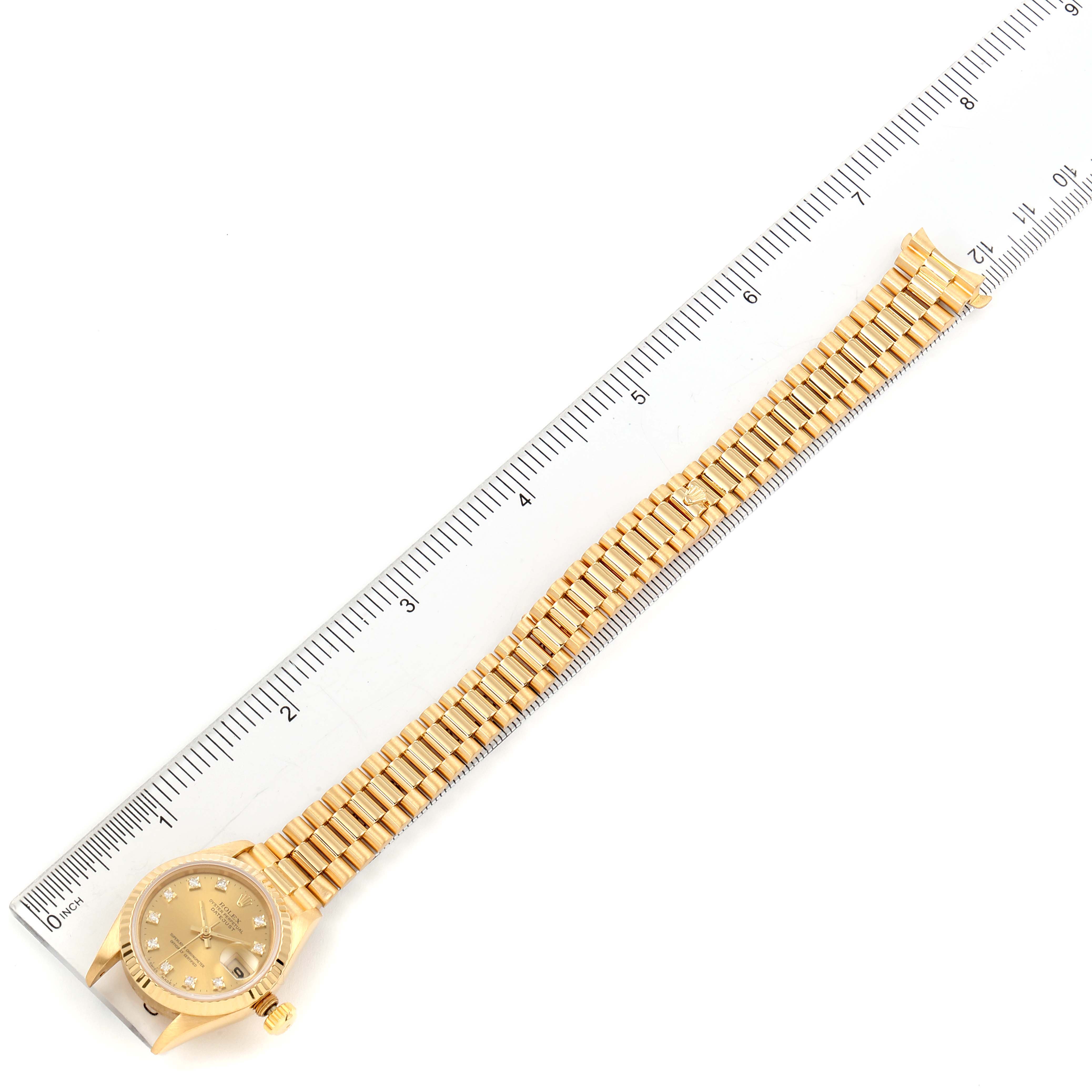 The image shows a Rolex President 69178 Women
s Yellow Gold Champagne Dial 69178 Women
s Yellow Gold Champagne Dial watch laid flat alongside a ruler, highlighting its gold bracelet and face from a top-down angle.