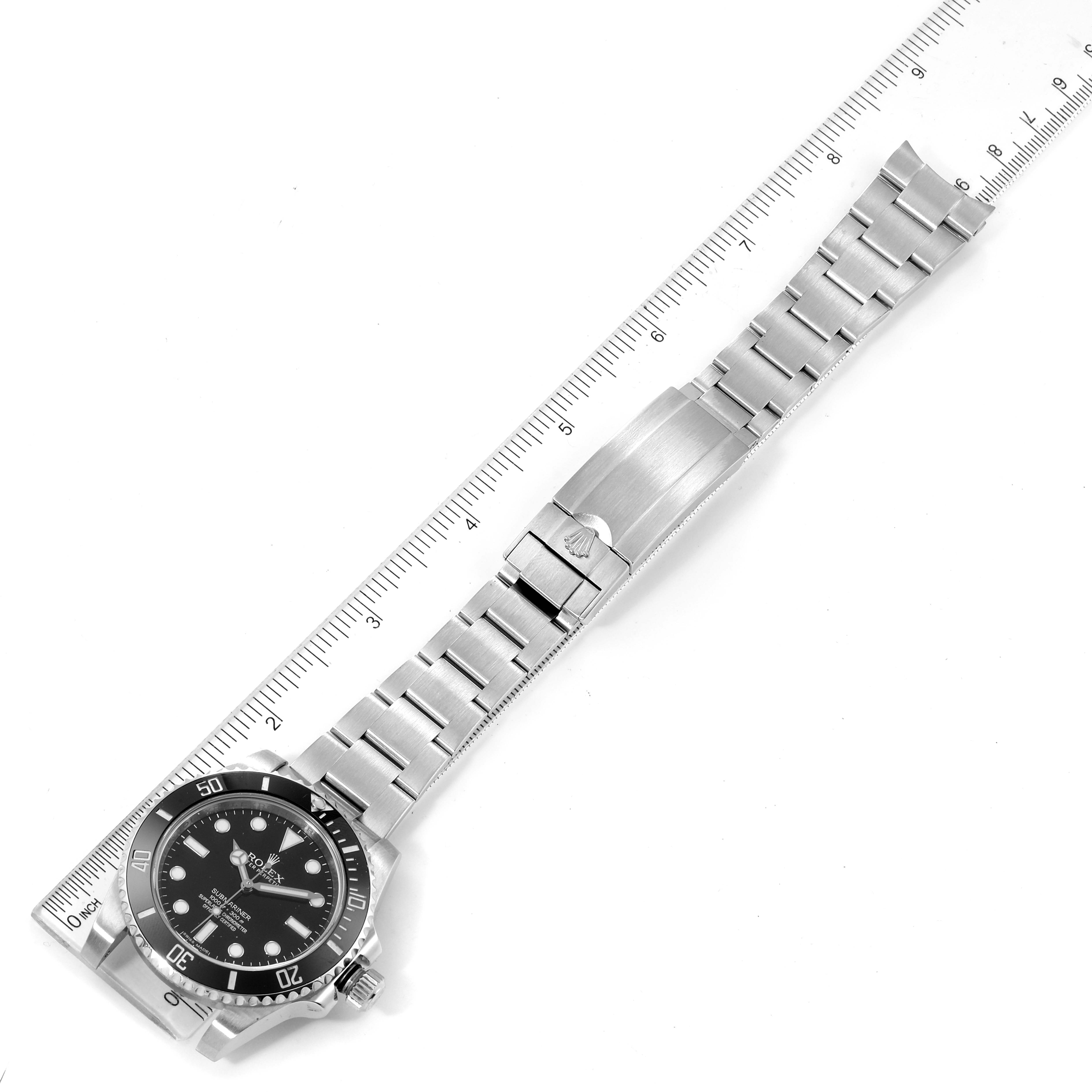 This image shows a Rolex Submariner 114060 Men
s Stainless Steel Black Dial 114060 Men
s Stainless Steel Black Dial watch laid flat, displaying the face, bezel, and full metal bracelet, next to a ruler for scale.