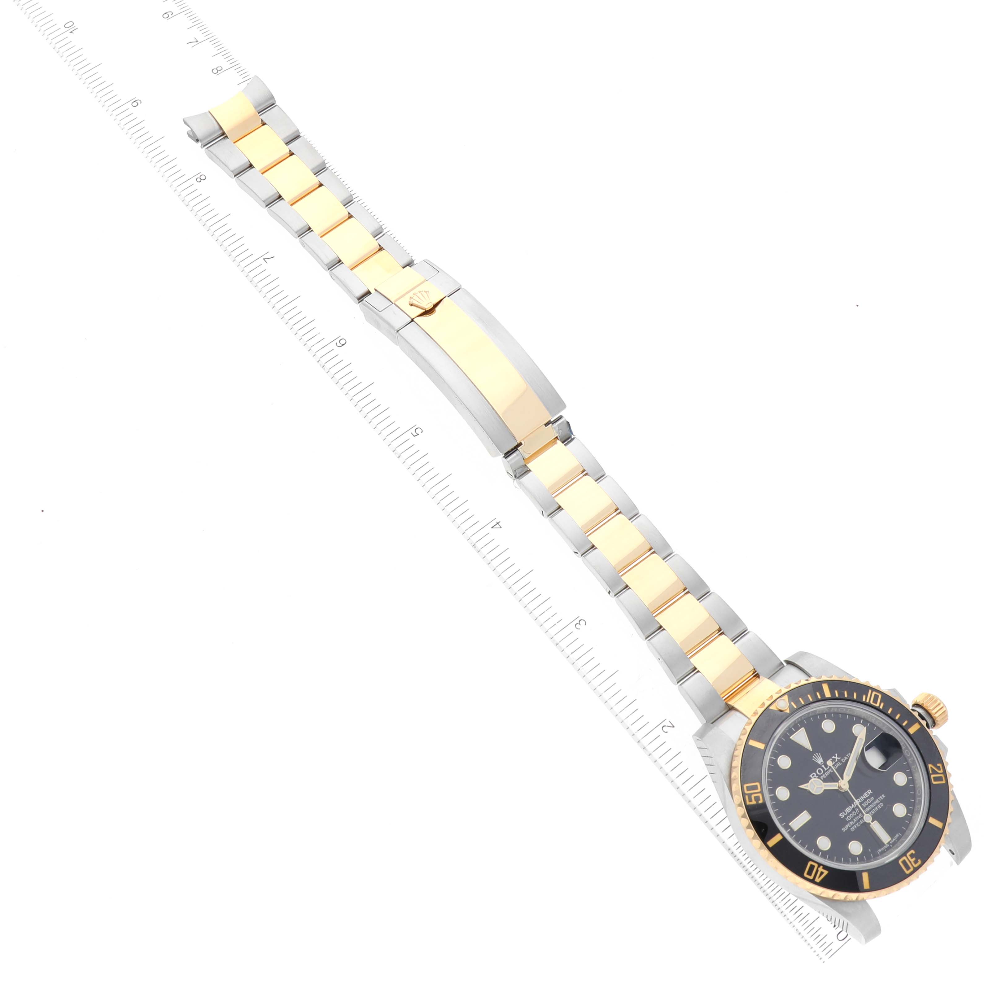 The image shows a top-down view of the Rolex Submariner 116613LN Men
s Steel and Gold (two tone) Black Dial 116613LN Men
s Steel and Gold (two tone) Black Dial watch, highlighting its face, two-tone bracelet, and clasp, placed next to a ruler.