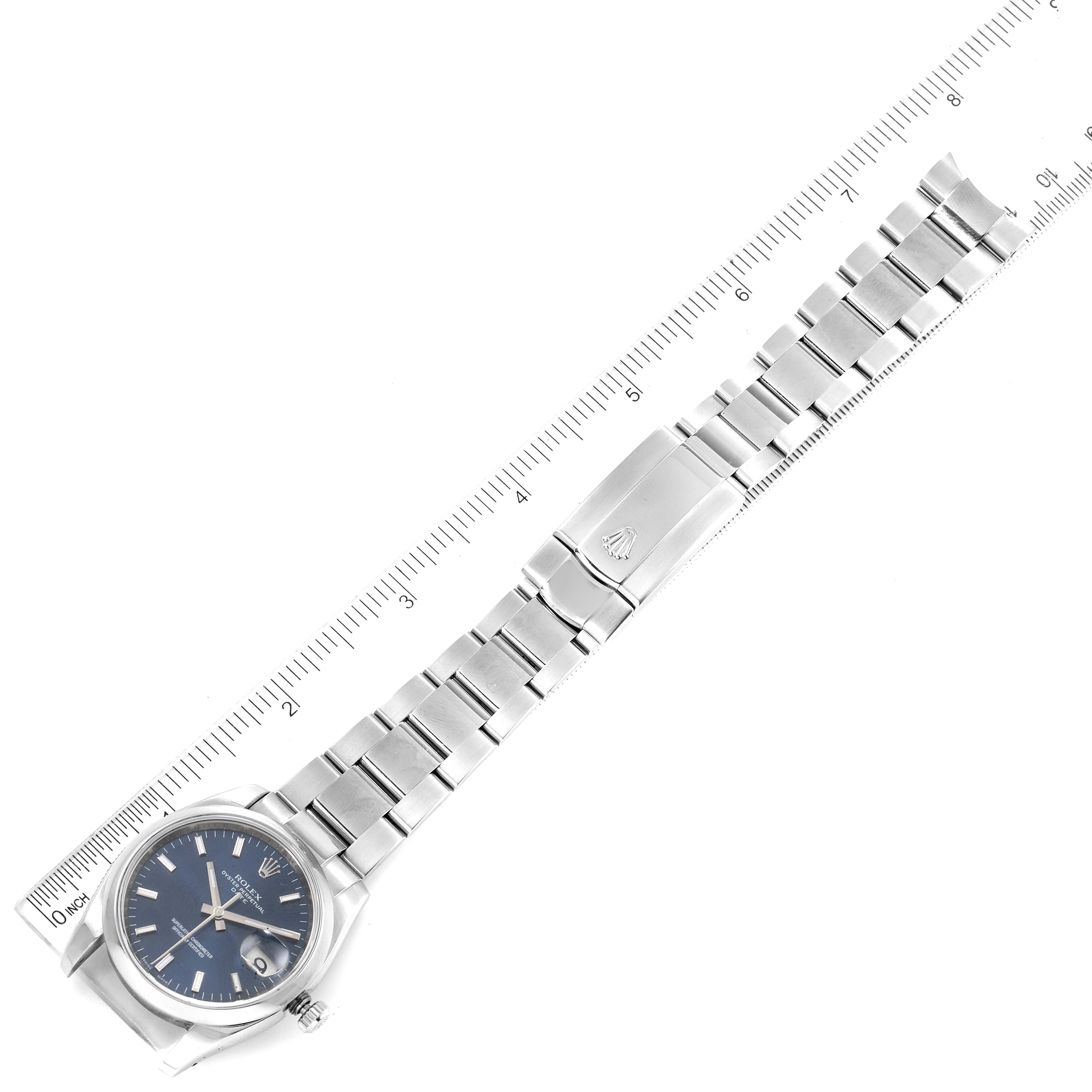 This image shows a top-down view of a Rolex Date 115200 Men's Stainless Steel Blue Dial 115200 Men's Stainless Steel Blue Dial model watch with a full view of its metal bracelet and clasp alongside a ruler for scale.