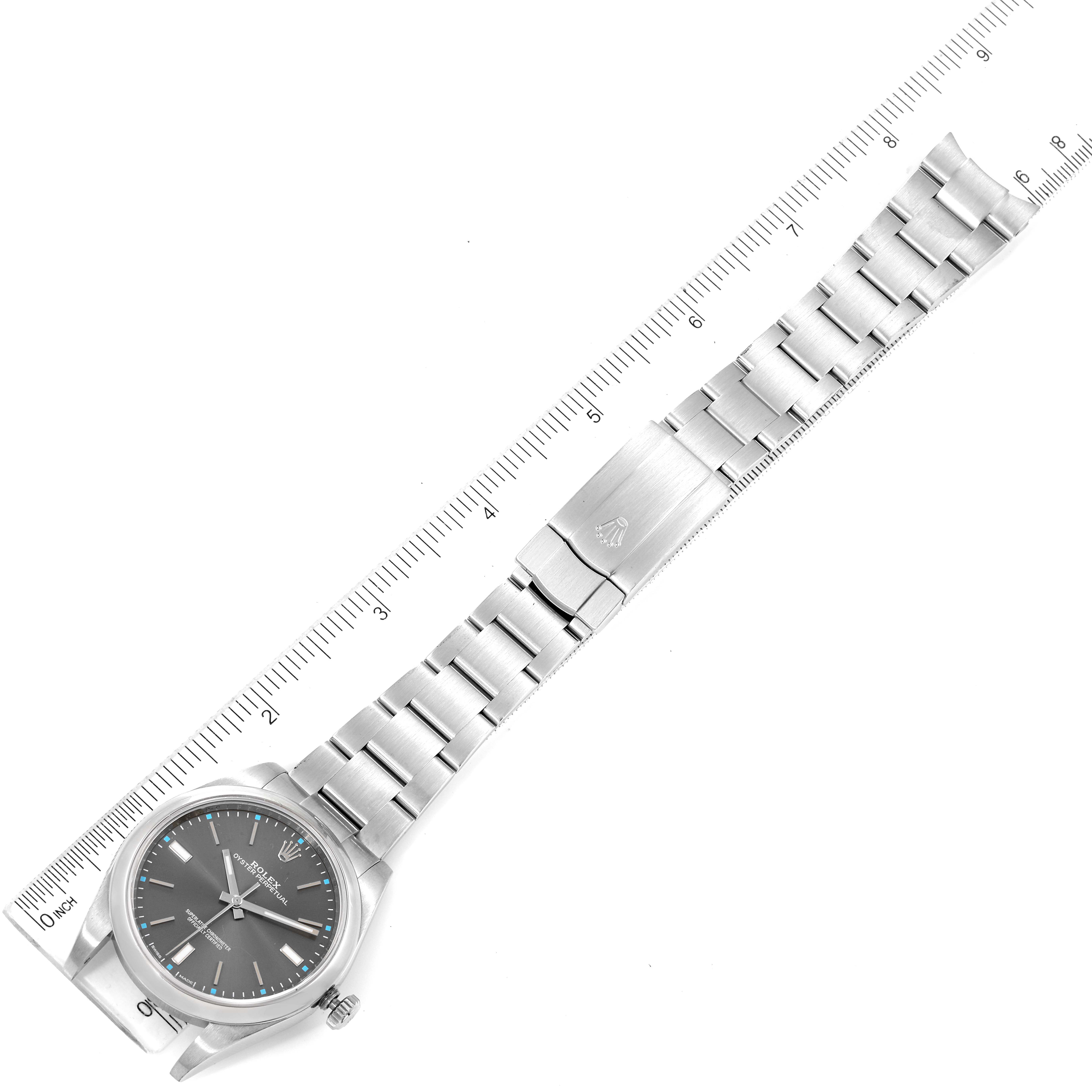 The image shows a top-down view of a Rolex Oyster Perpetual 114300 Men's Stainless Steel Grey Dial 114300 Men's Stainless Steel Grey Dial watch, focusing on the face, bracelet, and deployment clasp with a ruler for scale.