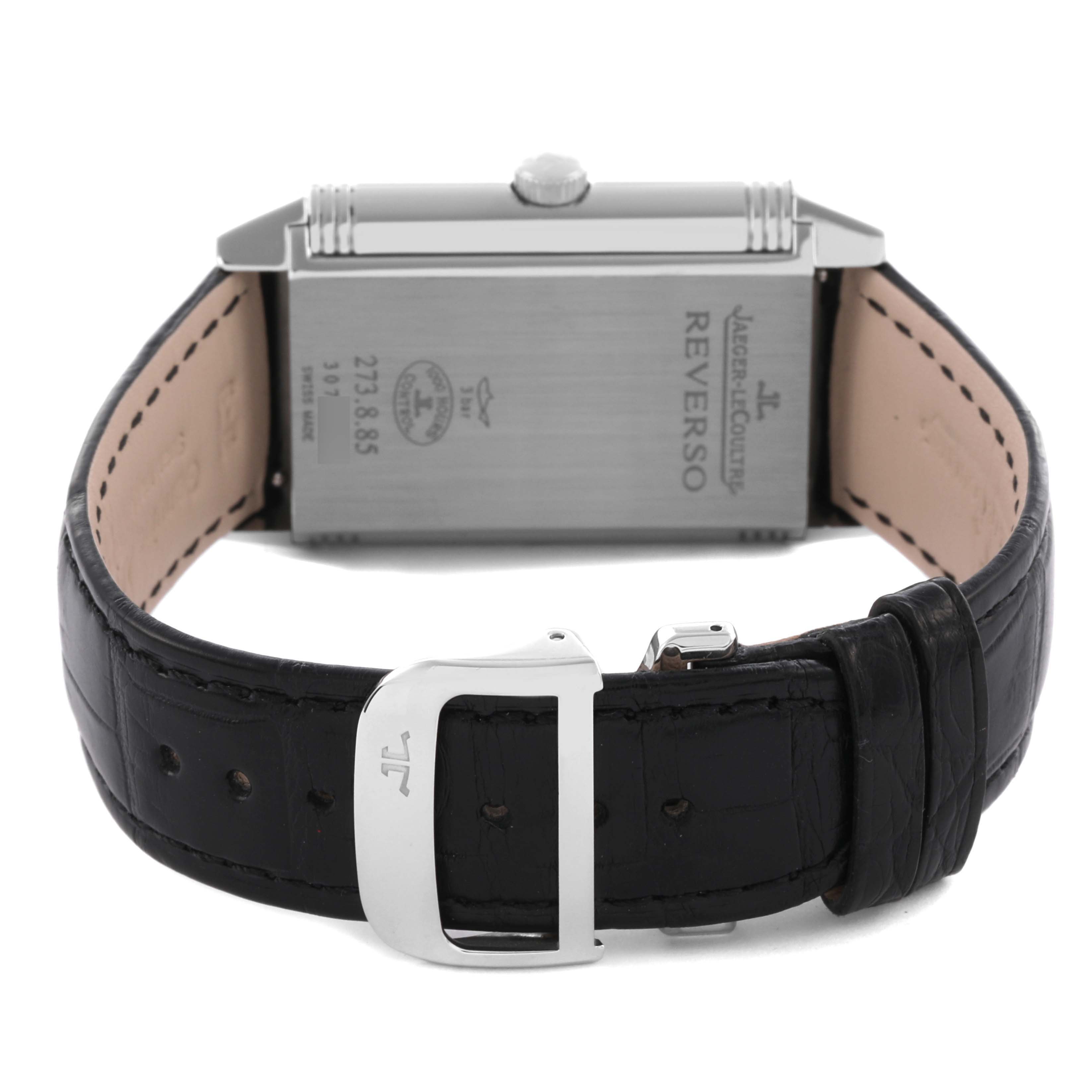 The Jaeger-LeCoultre Reverso watch is shown from the back, highlighting the case back, crown, and leather strap with a buckle.
