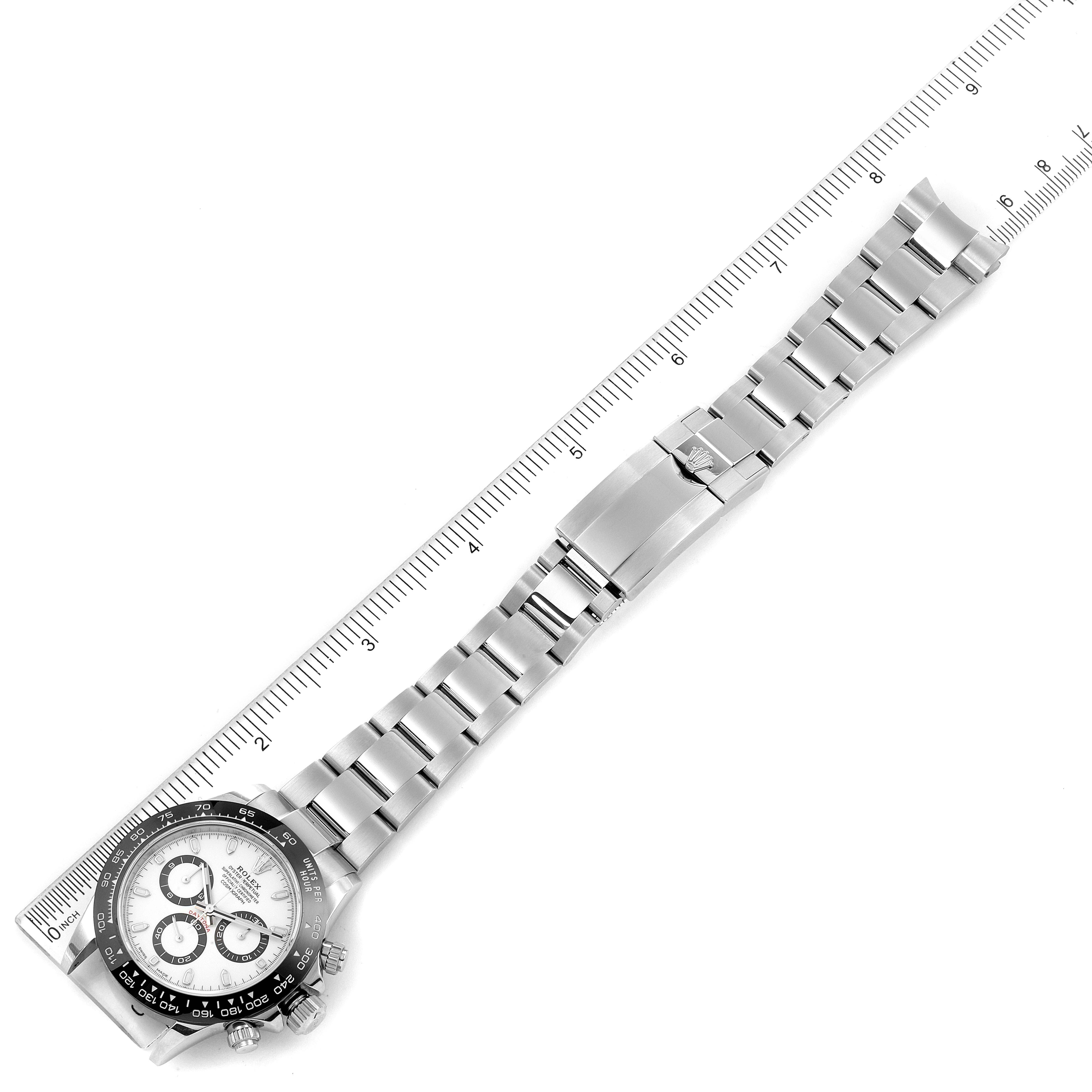 The Rolex Daytona 116500 Men's Stainless Steel White Dial 116500 Men's Stainless Steel White Dial watch is shown from a top-down angle, displaying the dial, bracelet, and clasp next to a measuring scale.