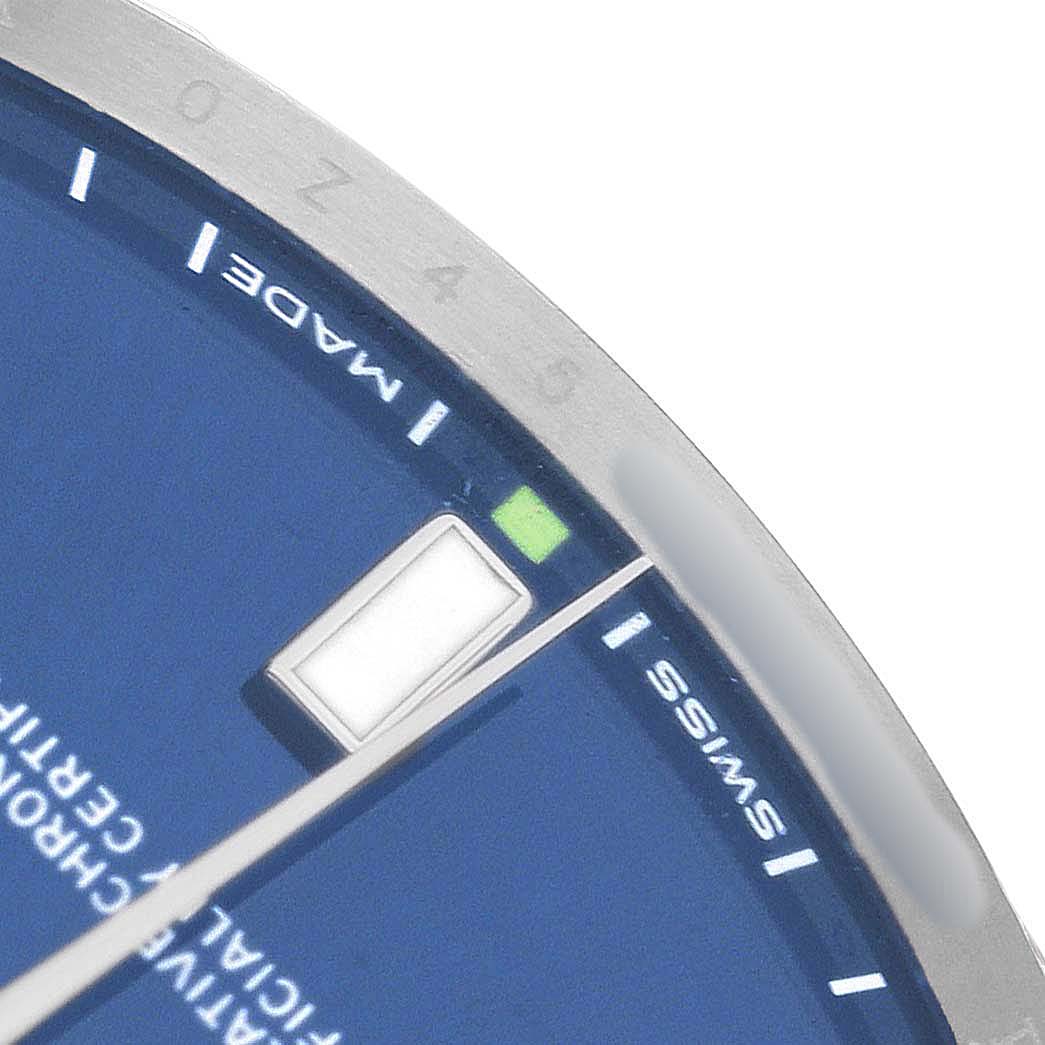 The image shows a close-up of the dial and bezel on a Rolex Oyster Perpetual 114300 Men's Stainless Steel Blue Dial, highlighting an hour marker and the text "SWISS MADE."