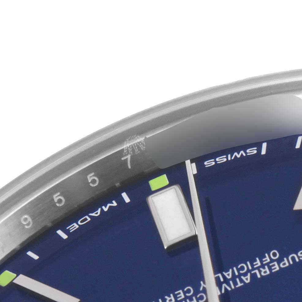 This close-up shot of the Rolex Oyster Perpetual 114300 Men's Stainless Steel Blue Dial 114300 Men's Stainless Steel Blue Dial shows part of the dial, indices, and a segment of the bezel around the 7 o'clock position.
