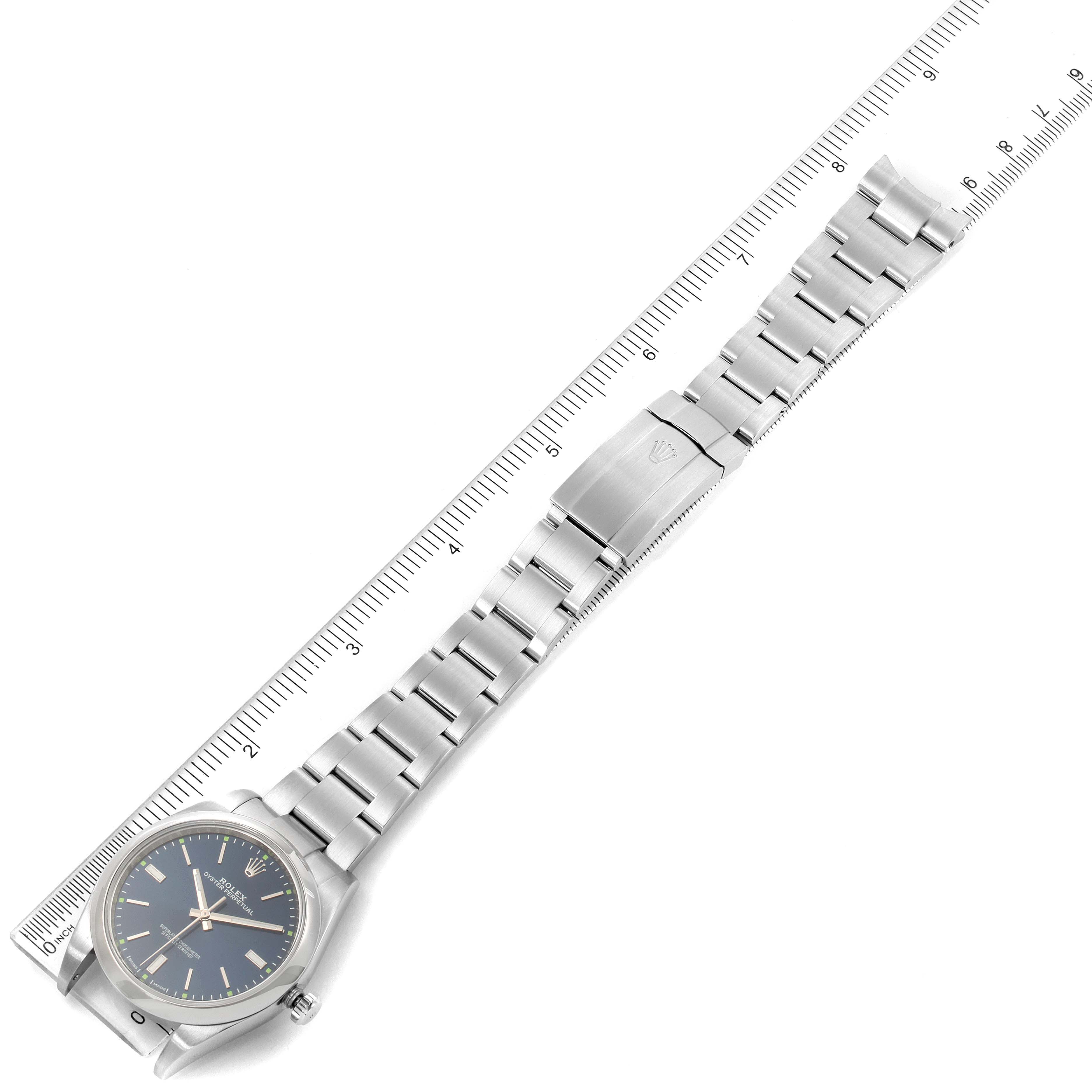 The image shows a top-down view of a Rolex Oyster Perpetual 114300 Men's Stainless Steel Blue Dial 114300 Men's Stainless Steel Blue Dial watch, including the face, bracelet, and clasp, aligned with a ruler.