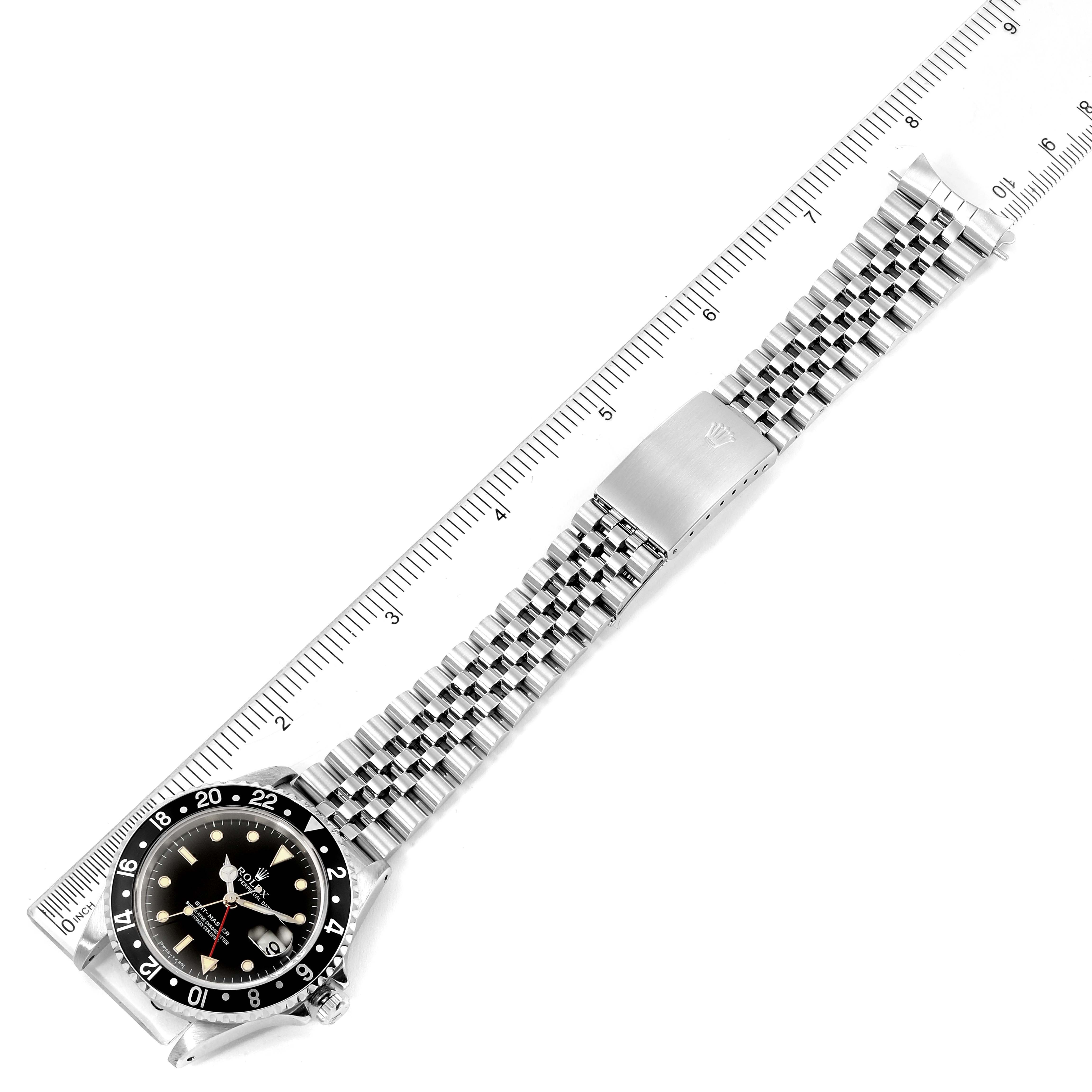 The image shows a top view of a Rolex GMT-Master 16700 Men
s Stainless Steel Black Dial 16700 Men
s Stainless Steel Black Dial watch, highlighting its dial, bezel, and bracelet laid alongside a ruler.