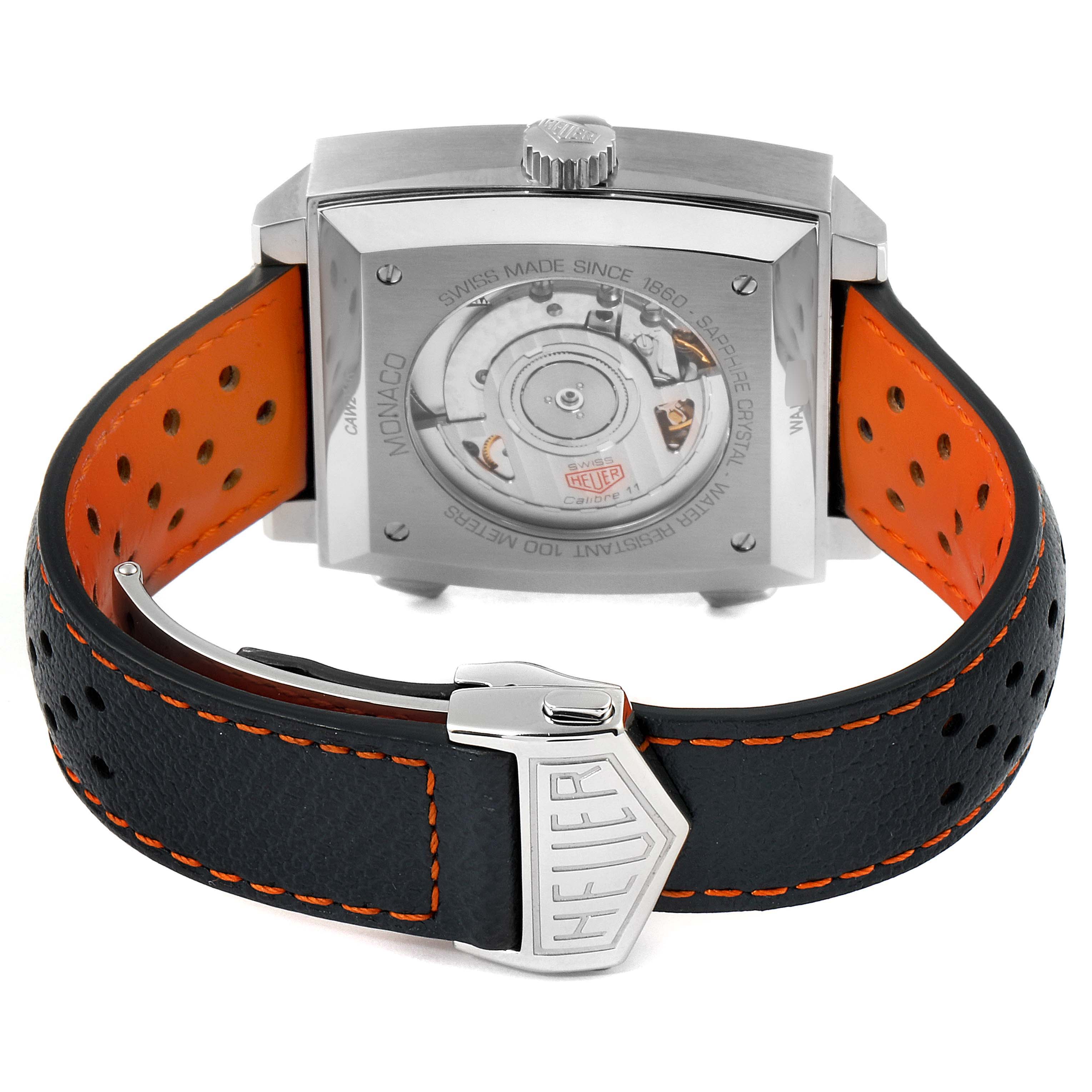 The image shows the back view of a Tag Heuer Monaco CAW211R.FC6401 Men's Stainless Steel Blue Dial CAW211R.FC6401 Men's Stainless Steel Blue Dial watch, displaying its movement and the clasp on the orange and black strap.