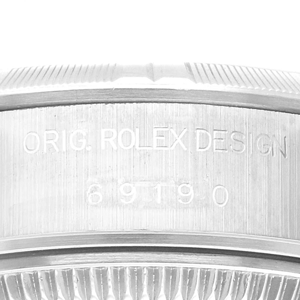 This image is a close-up of the side of a Rolex Date 69190 Women's Stainless Steel Blue Dial 69190 Women's Stainless Steel Blue Dial model watch, showing the engraved "ORIG. ROLEX DESIGN" text and part number.