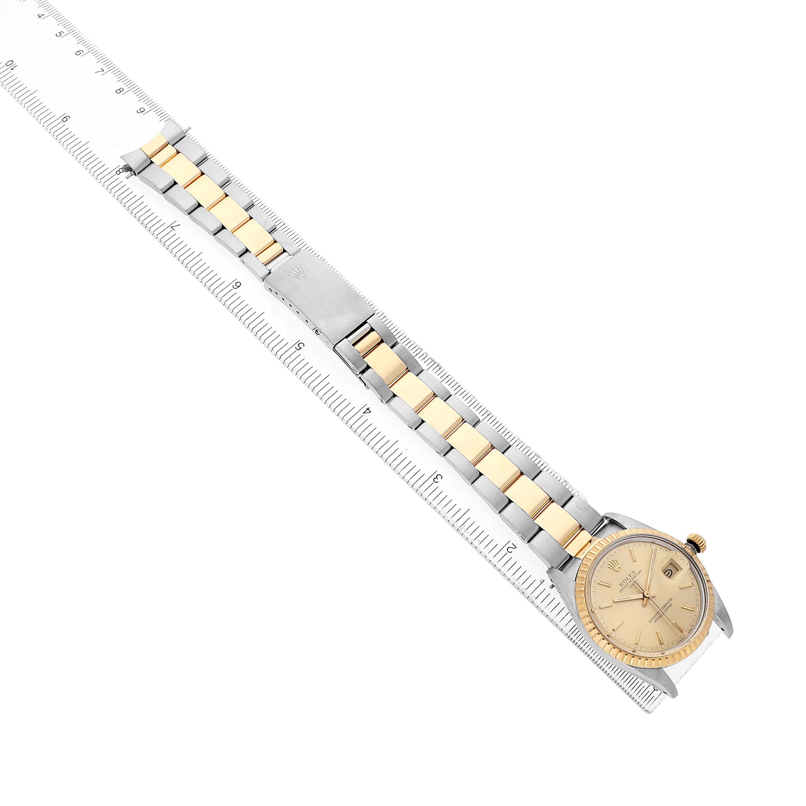 The Rolex Date 15053 Men's Steel and Gold (two tone) Champagne Dial watch is shown from an angular top view, highlighting the face and two-tone bracelet alongside a ruler.