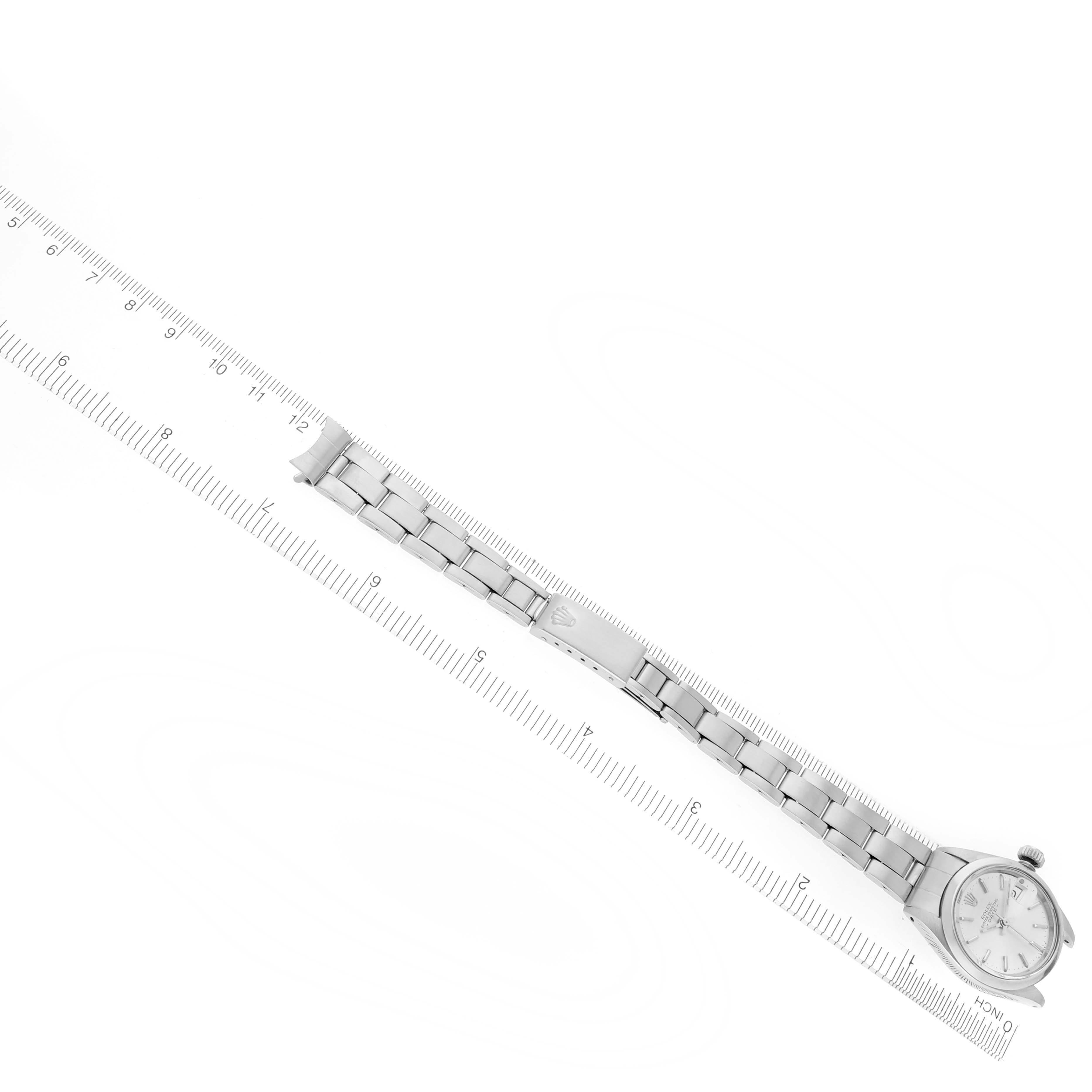 The Rolex Date 6916 Women's Stainless Steel Silver Dial 6916 Women's Stainless Steel Silver Dial watch is shown from a top-down angle, displaying the face, bracelet, and clasp alongside a ruler.