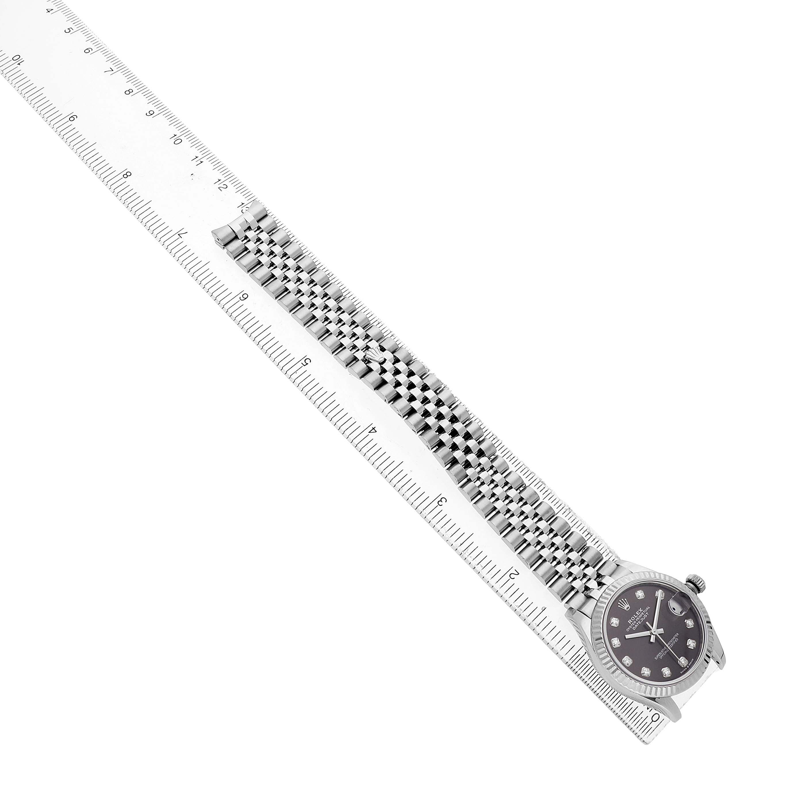 The Rolex Datejust 278274 Women's Stainless Steel Grey Dial watch is shown from an overhead angle, highlighting its face, bracelet, and compared in length to a ruler.