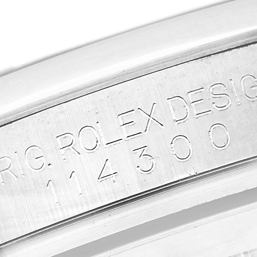 The image shows the engraved side of the case for a Rolex Oyster Perpetual 114300 Men's Stainless Steel Grey Dial 114300 Men's Stainless Steel Grey Dial, displaying the model number and "ROLEX DESIGN."
