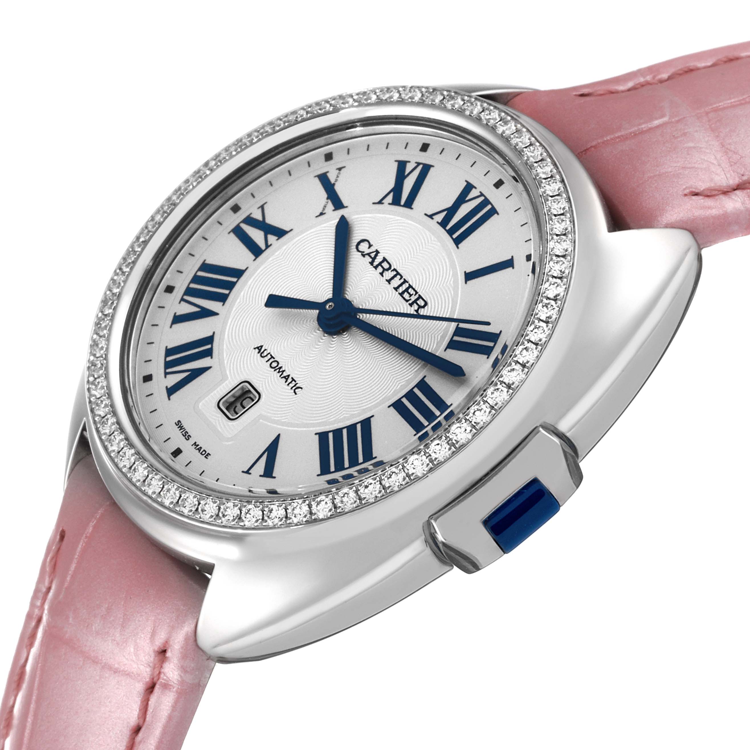 The Cartier Clé watch is displayed at a slight angle, showing its pink leather strap, diamond-studded bezel, and blue-accented crown.