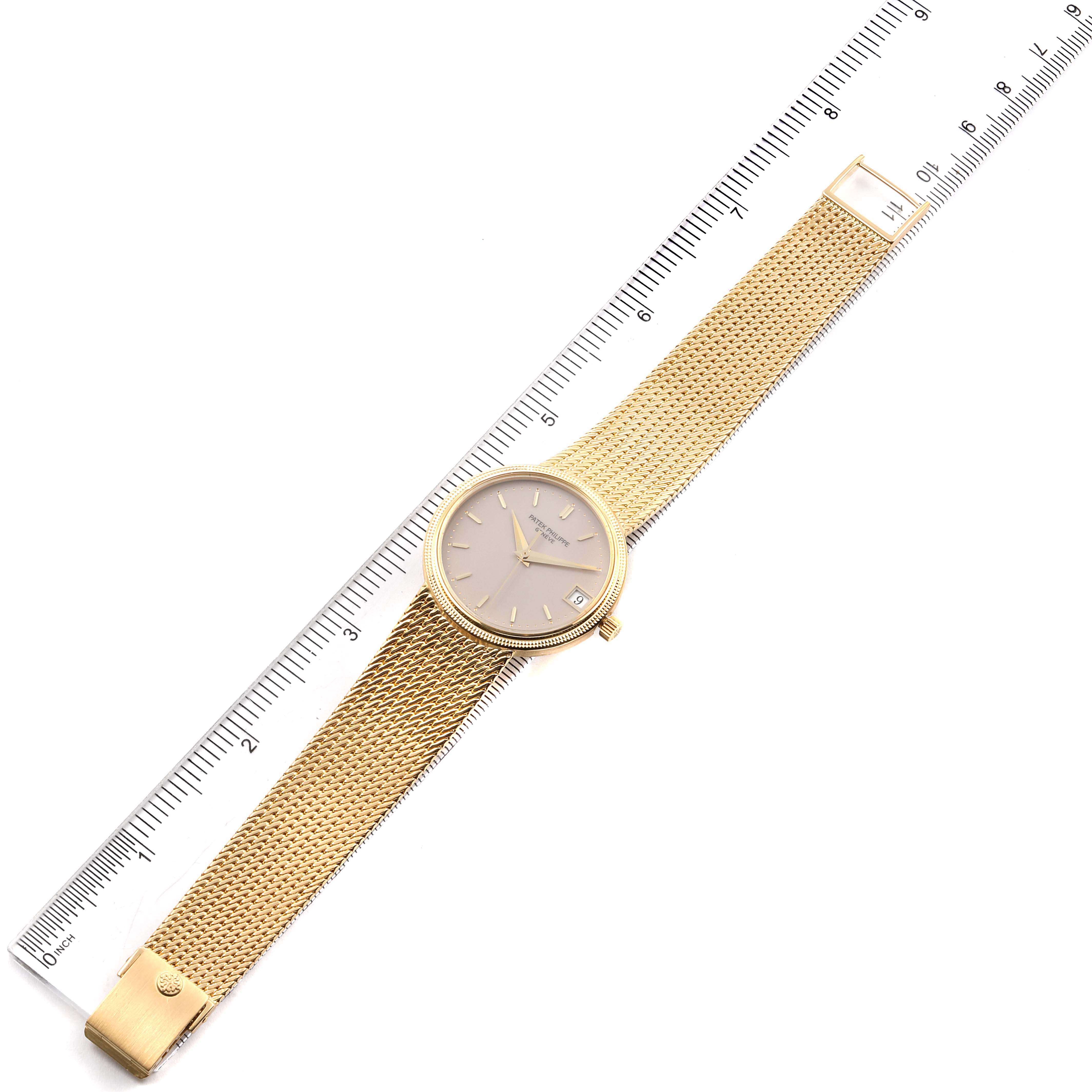 The image shows a top view of a Patek Philippe Calatrava 3802 Men's Yellow Gold Beige Dial 3802 Men's Yellow Gold Beige Dial watch with a gold mesh strap next to a ruler.