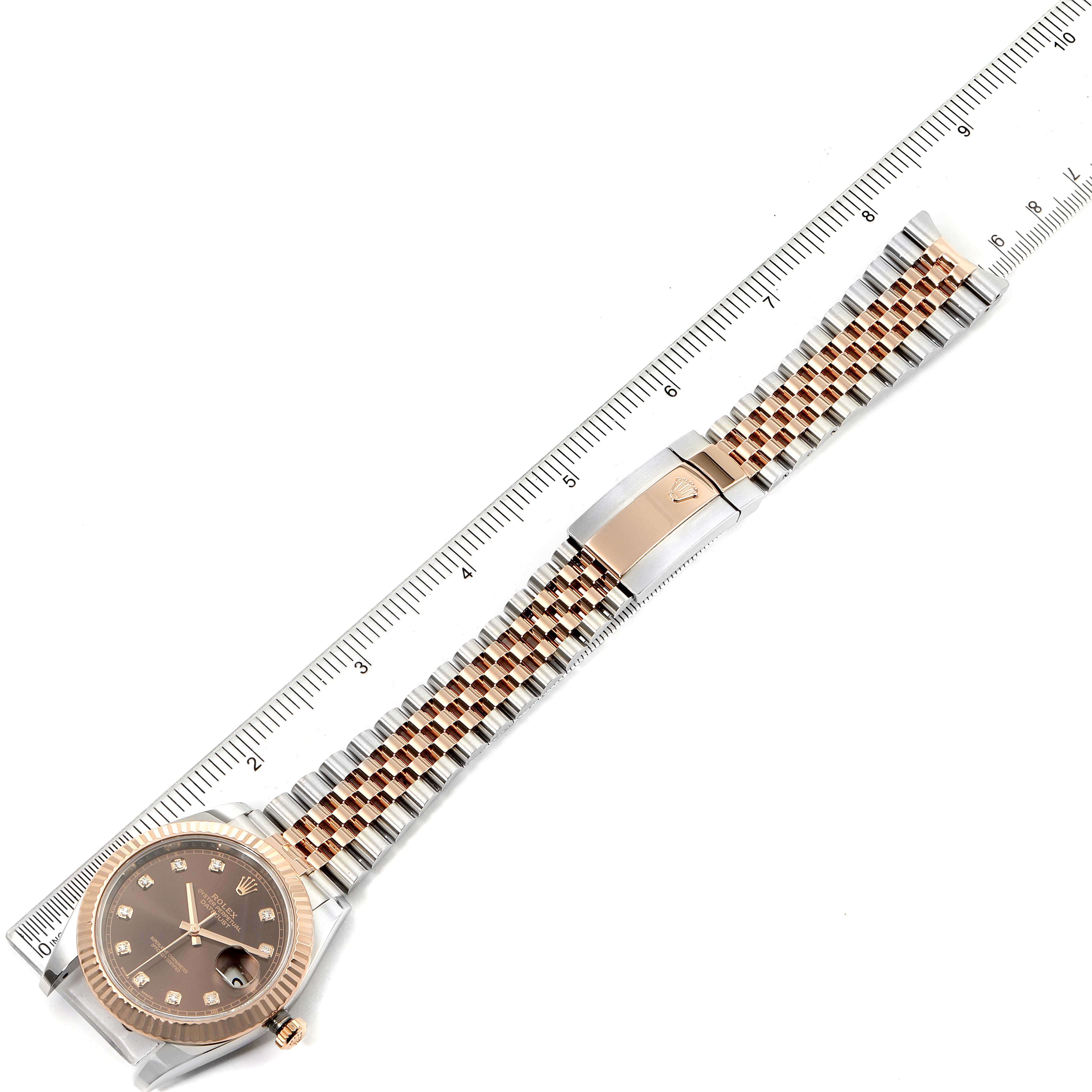 The image shows a top-down view of a Rolex Datejust 41 126331 Men's Steel and Gold (two tone) Brown Dial 126331 Men's Steel and Gold (two tone) Brown Dial watch, including its dial, bezel, and jubilee bracelet next to a ruler.