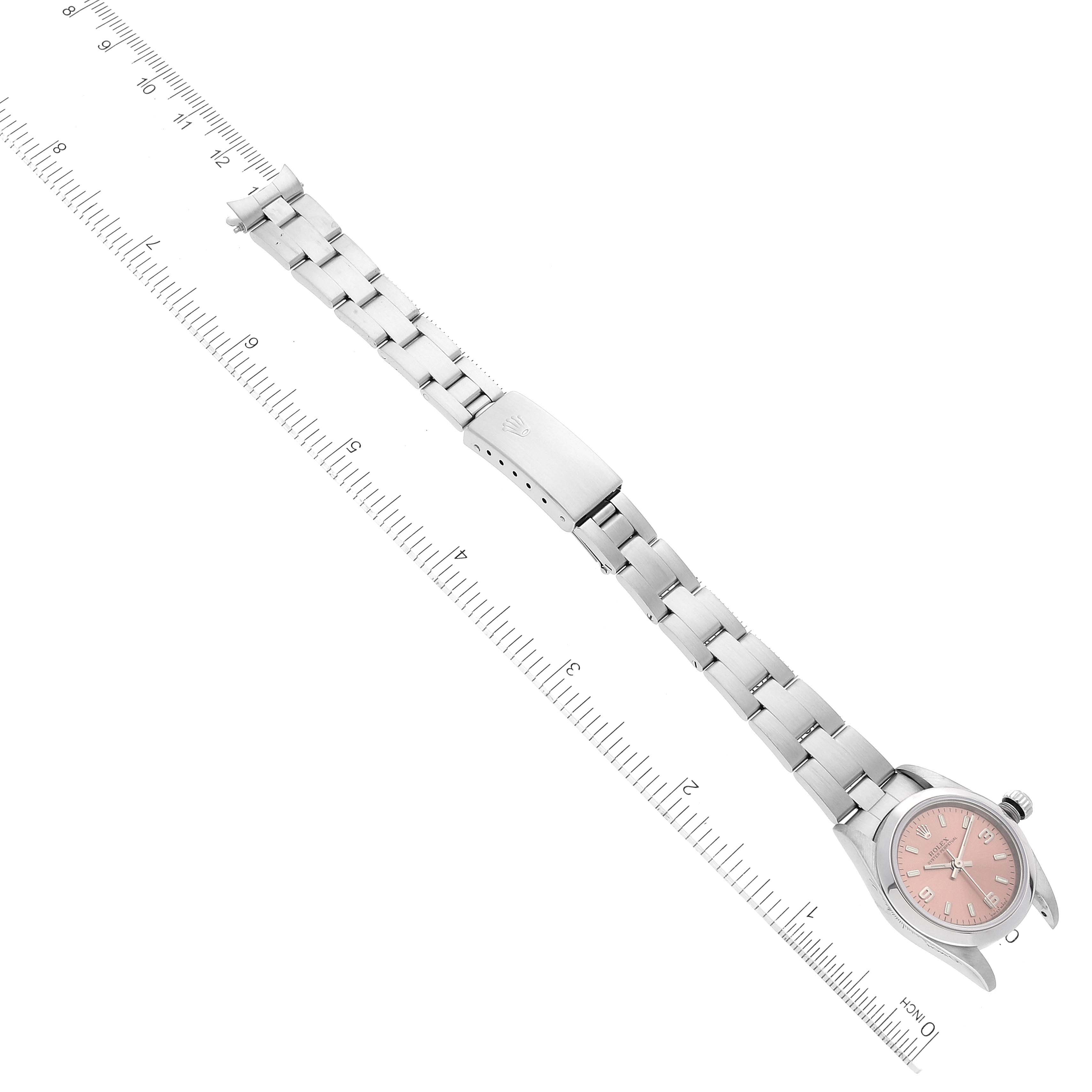 The image shows a Rolex Oyster Perpetual 76080 Women
s Stainless Steel Pink Dial 76080 Women
s Stainless Steel Pink Dial watch with its full metal bracelet and clasp, laid flat beside a ruler.