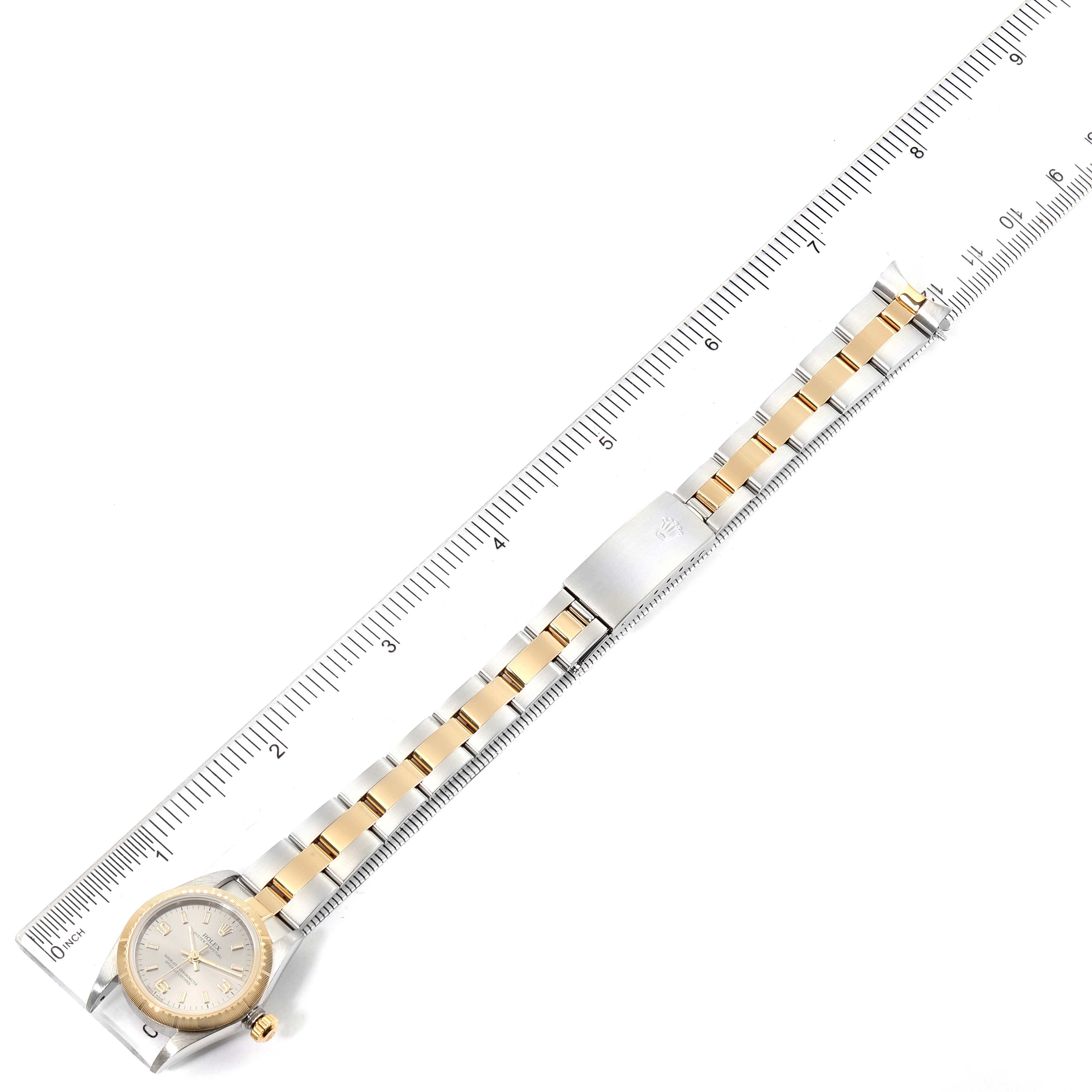 A Rolex Oyster Perpetual 76243 Women's Steel and Gold (two tone) Silver Dial 76243 Women's Steel and Gold (two tone) Silver Dial watch is shown laid flat, displaying its dial, bezel, and bracelet alongside a measurement ruler.