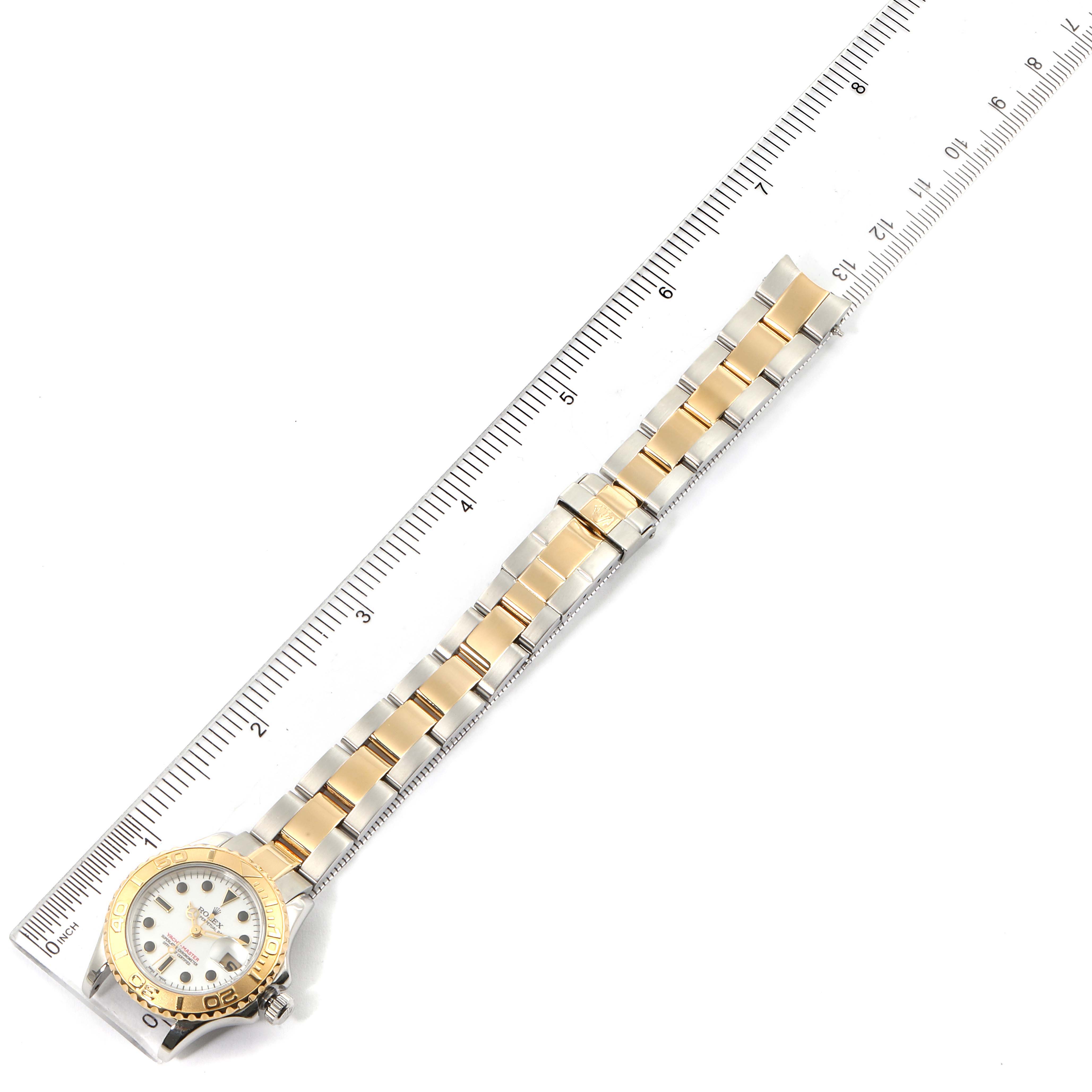 The image shows a top view of a Rolex Yacht-Master 169623 Women's Steel and Gold (two tone) White Dial 169623 Women's Steel and Gold (two tone) White Dial watch with its full two-tone bracelet and part of a ruler beside it.